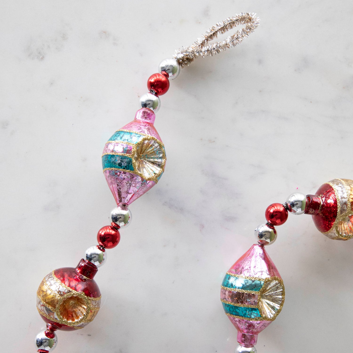 The Retro Tinsel and Glass Finial Garland on a marble table, showing its glittery details and tinsel loop.