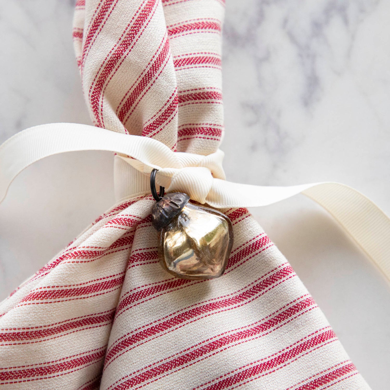 Embossed Antique Gold Mercury Glass Ornament tied to a red stripe napkin.