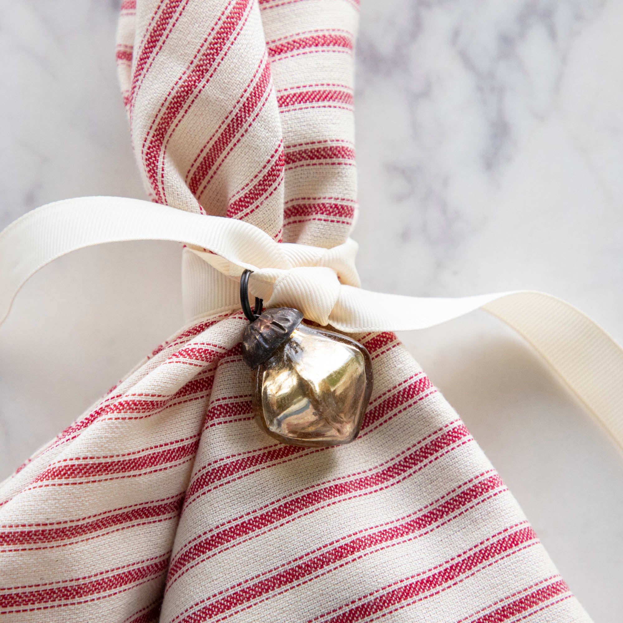 Embossed Antique Gold Mercury Glass Ornament tied to a red stripe napkin.