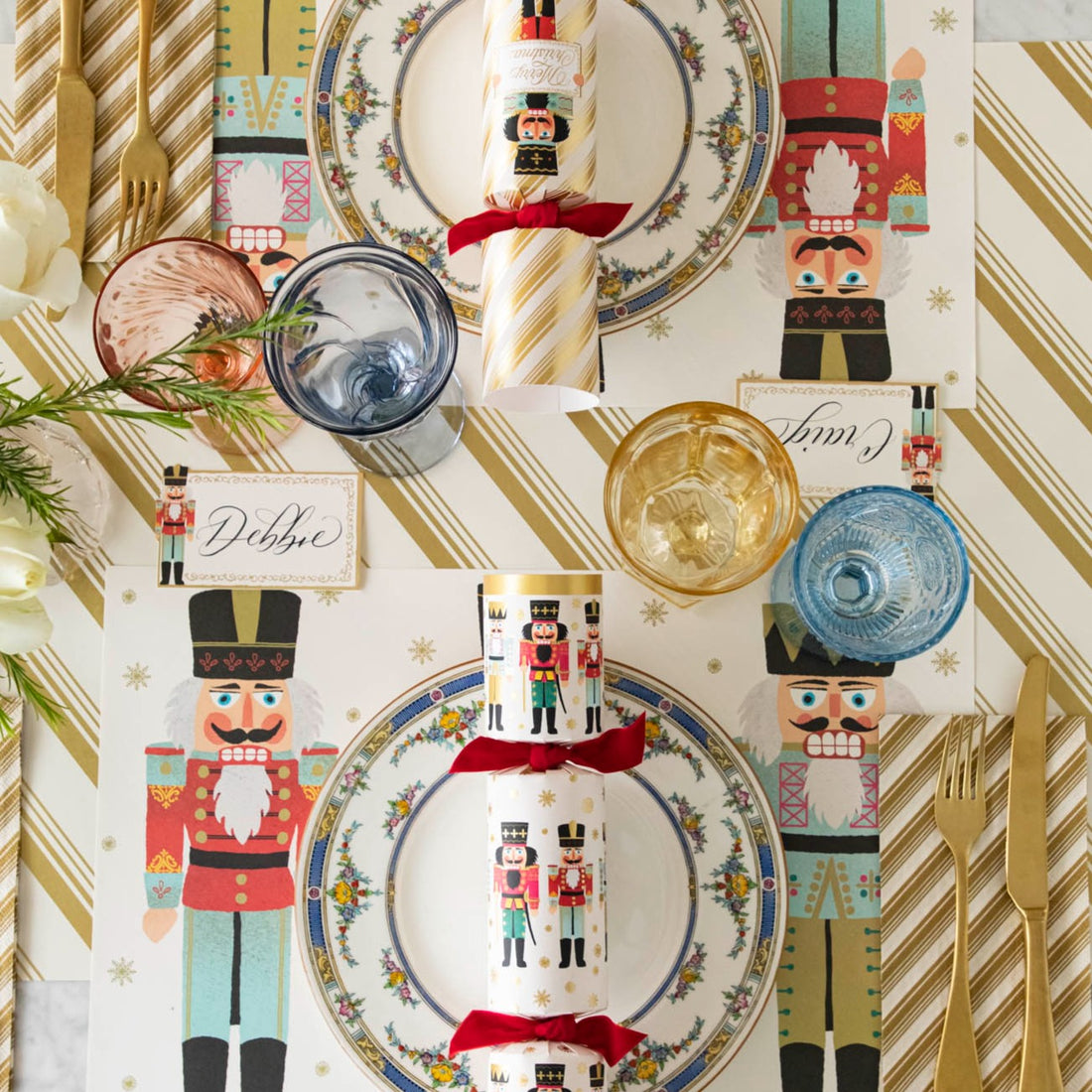 An elegant table setting with the Gold Peppermint Stripe Runner under the Nutcracker Placemat, Gold Peppermint Stripe Guest Napkin and Nutcracker Place Card with the name &quot;Debbie&quot; written in cursive.