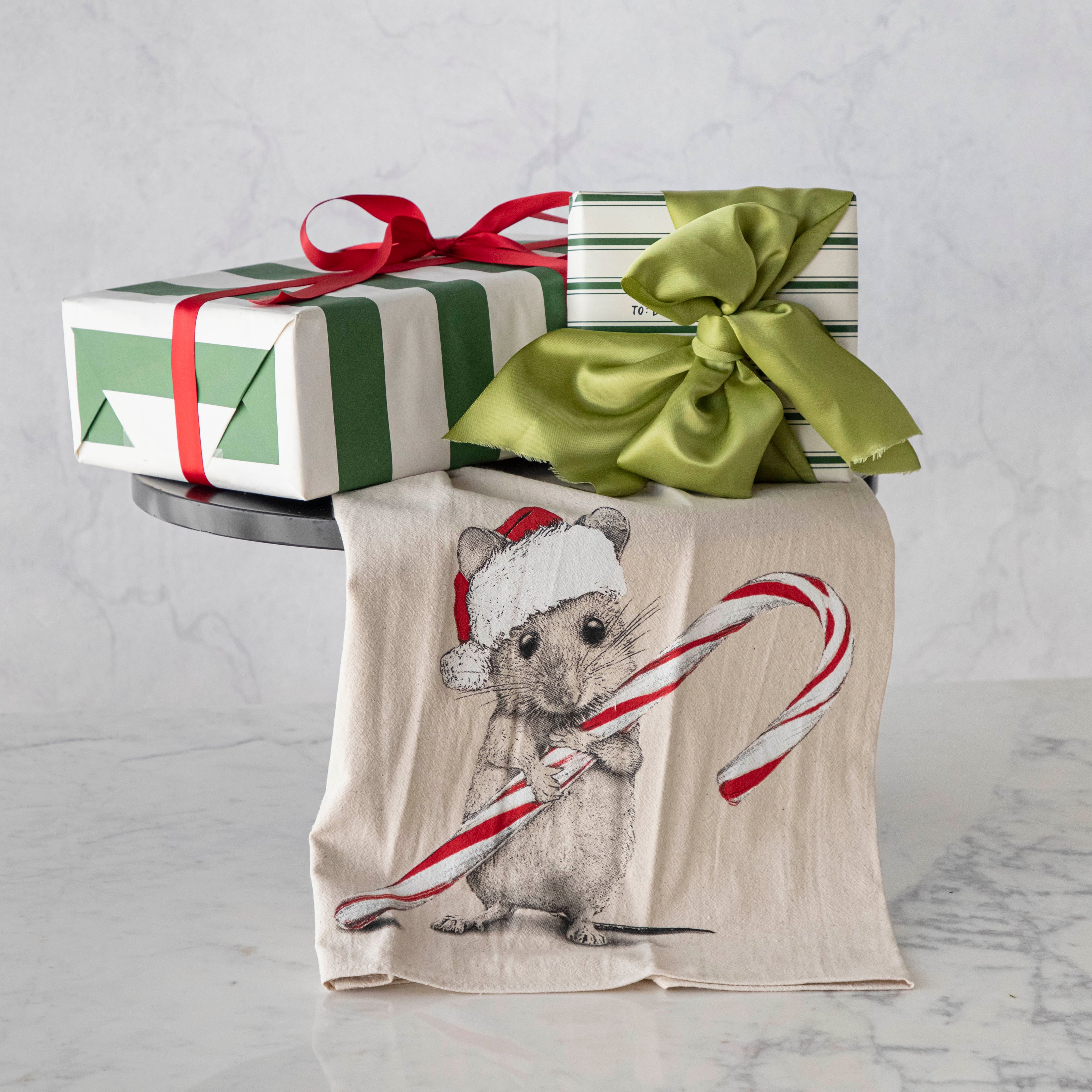 tea towel with mouse wearing a Santa hat holding a candy cane with wrapped gifts above it. 