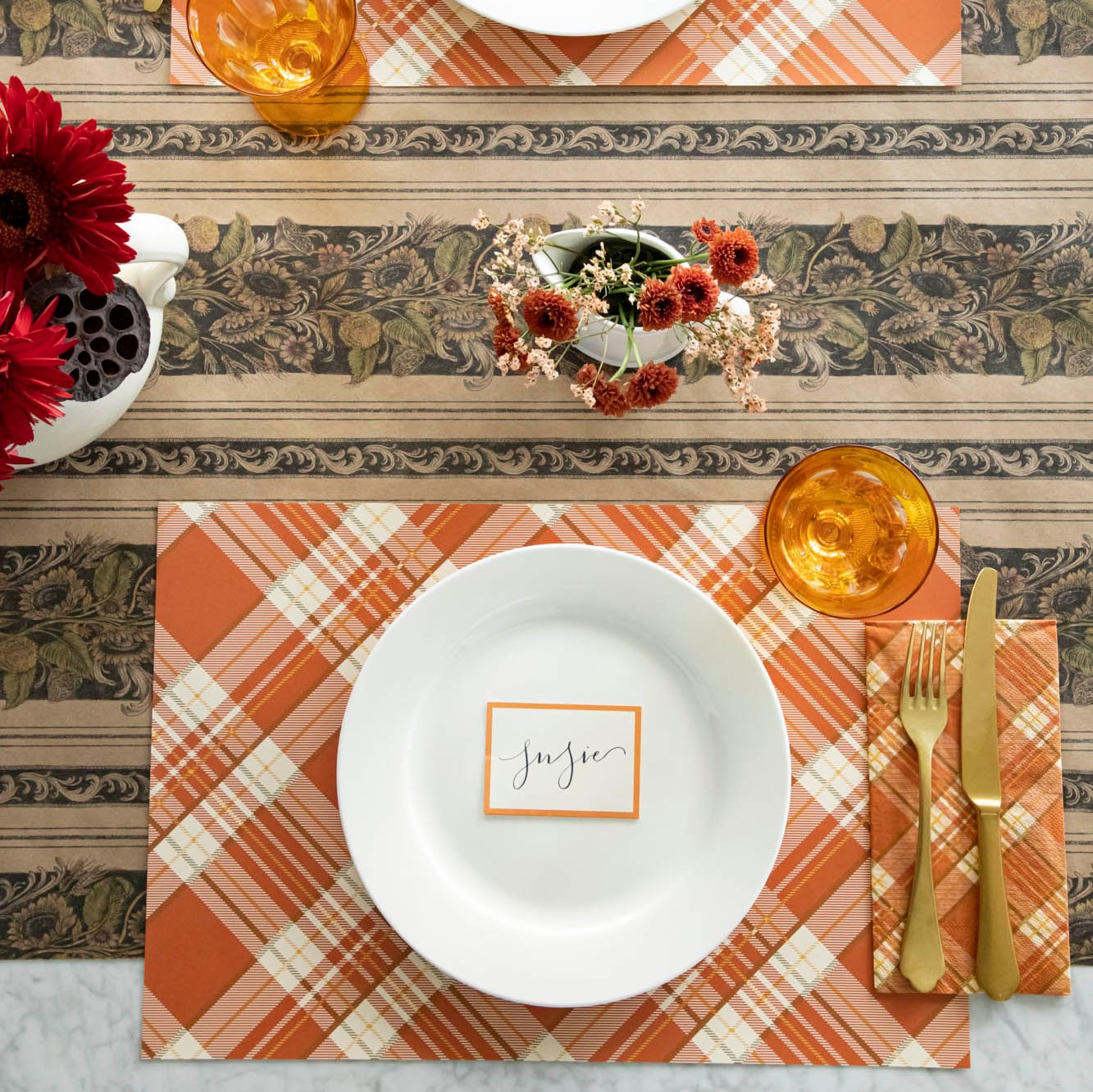 Orange Plaid Placemat on a Vintage Sunflower Runner with flowers, a white plate with an Orange Frame Place card on top, and gold silverware with an Amber colored glass.