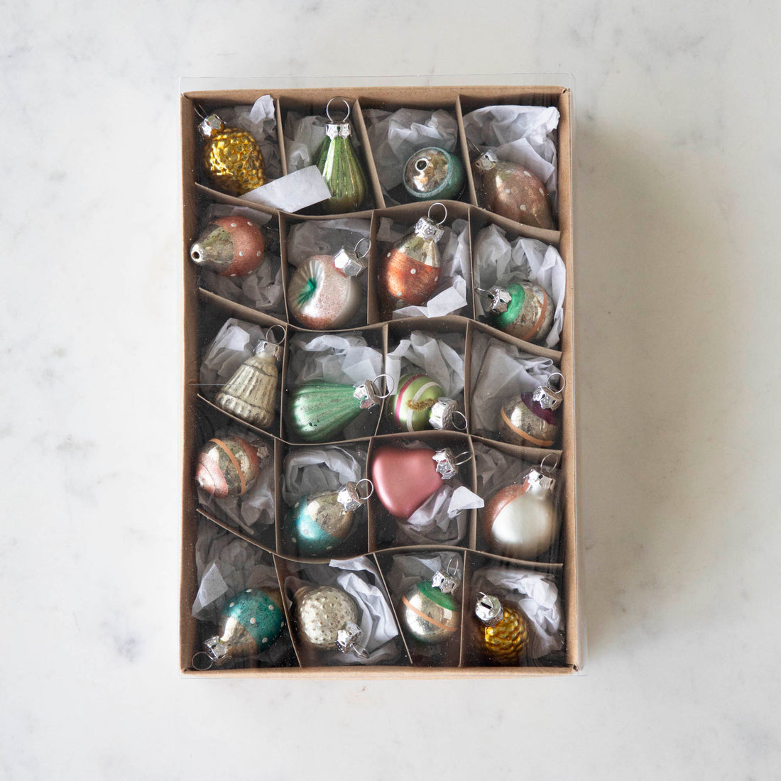 A set of 20 Multicolor Ornaments in a brown kraft box with tissue paper, on a marble table.