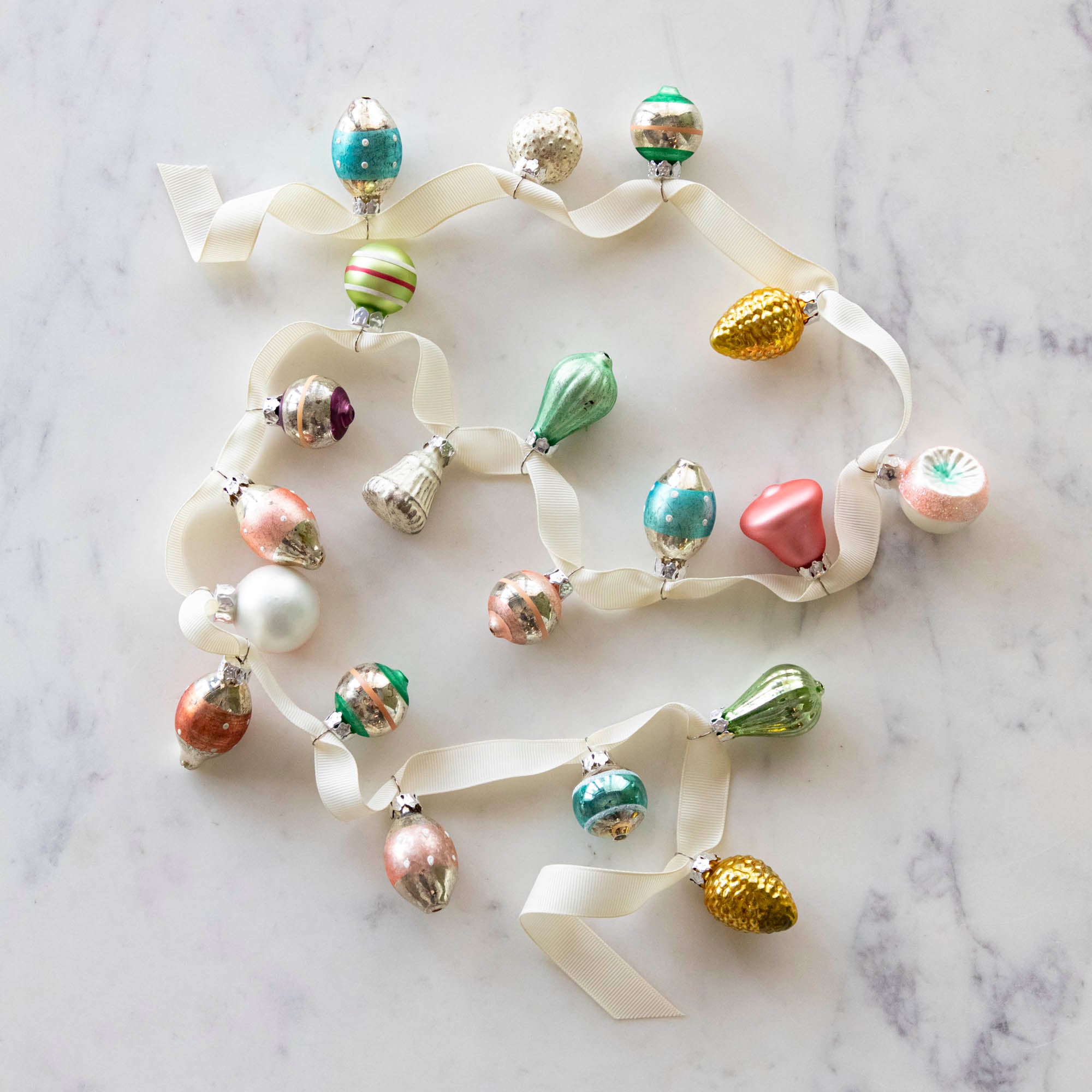 A set of 20 Multicolor Ornaments strung on a cream ribbon, on a marble table.