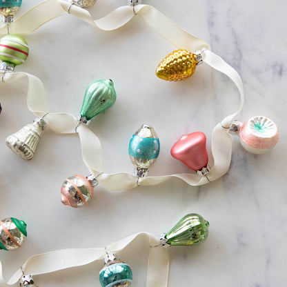 A set of 20 Multicolor Ornaments strung on a cream ribbon, on a marble table.