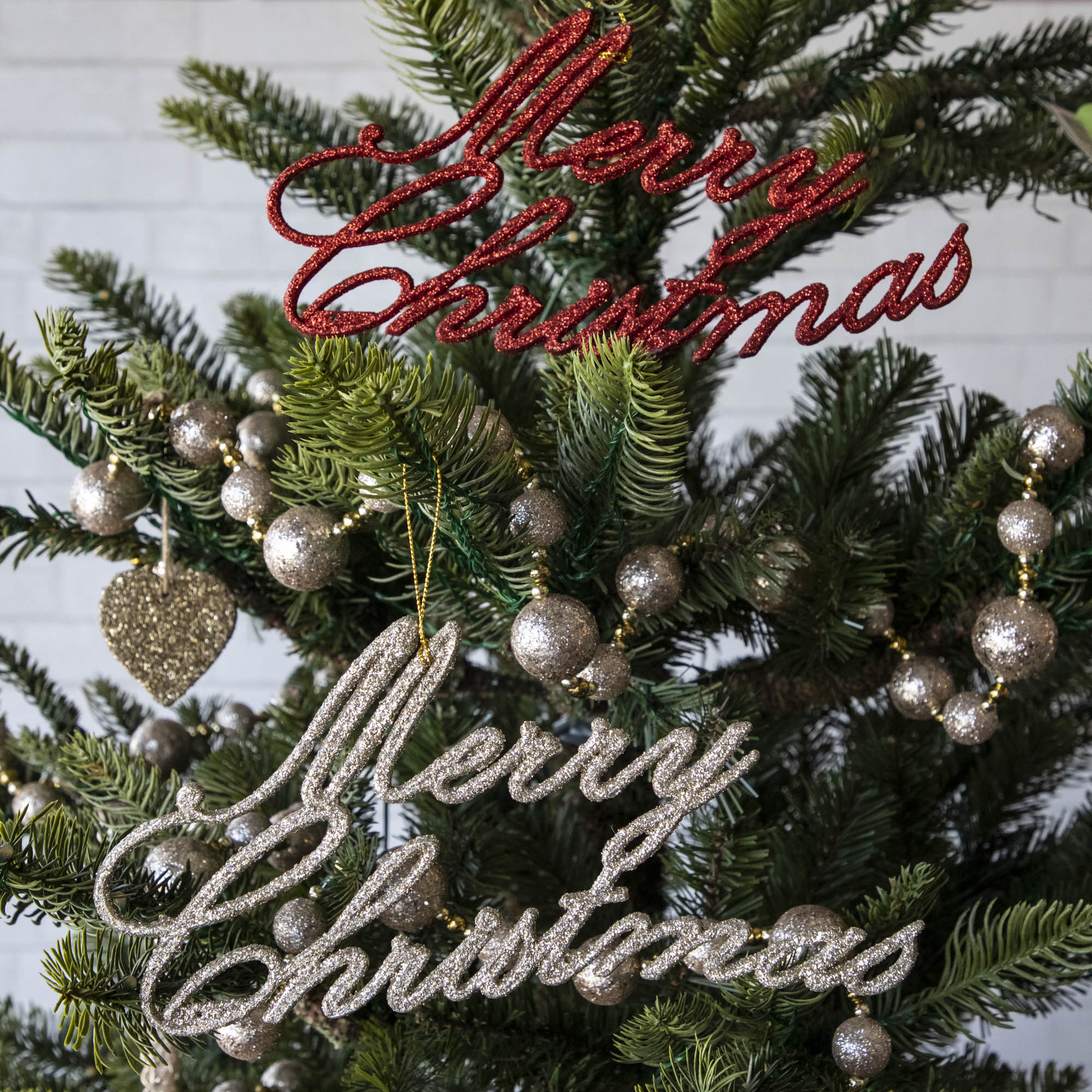 A red and champagne Merry Christmas Ornament hanging on a tree with other ornaments.