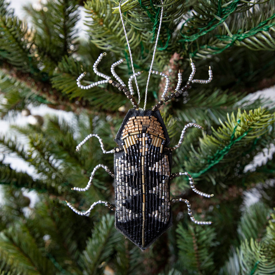 A holiday décor Christmas tree decorated with silver baubles and unique Shi Shi beaded insect ornaments.