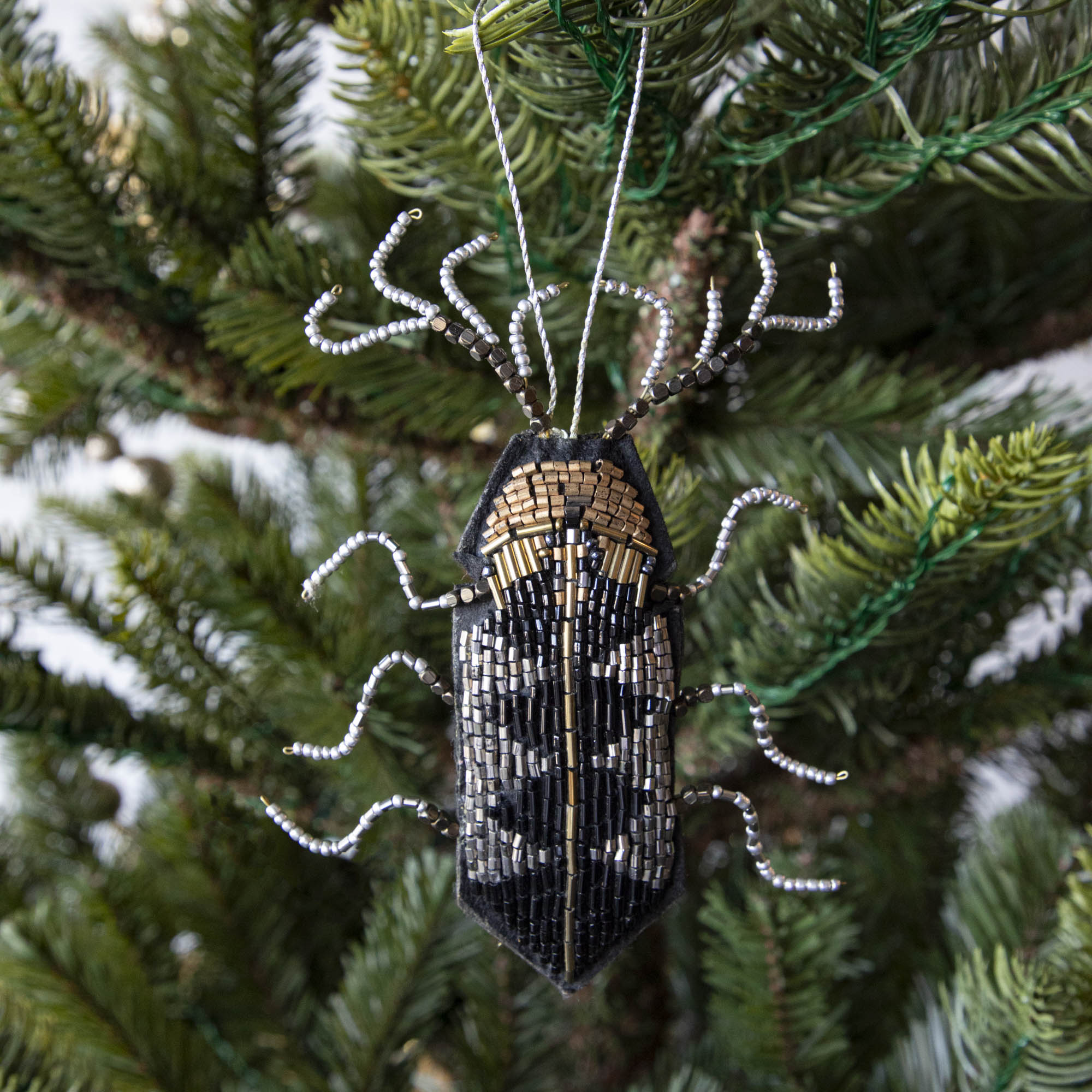 A holiday décor Christmas tree decorated with silver baubles and unique Shi Shi beaded insect ornaments.