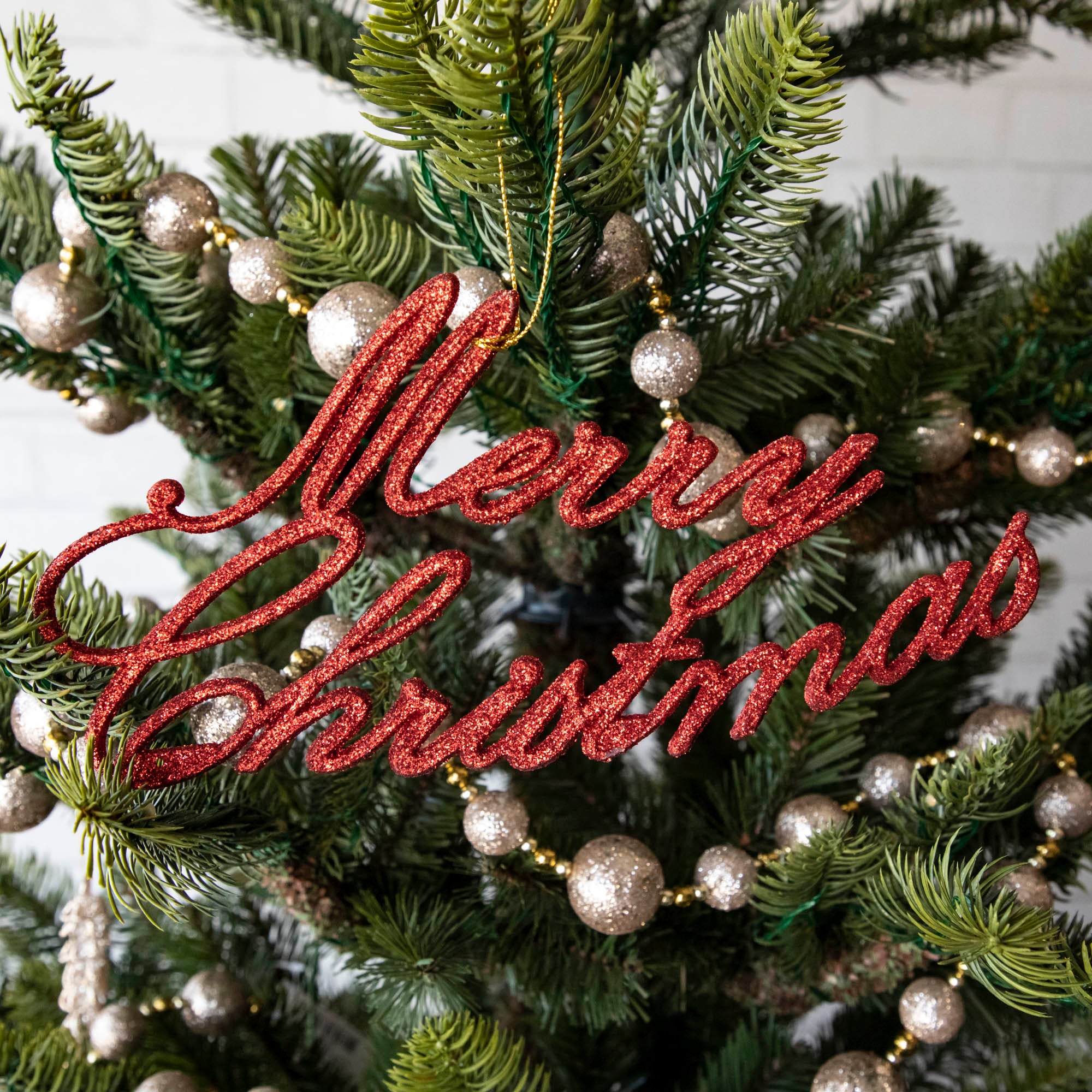 A Merry Christmas Red Ornament hanging on a tree with garland.