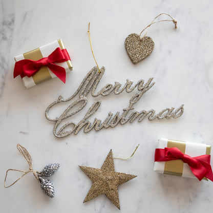 Champagne Merry Christmas ornament on a table with various other ornaments and wrapped gifts