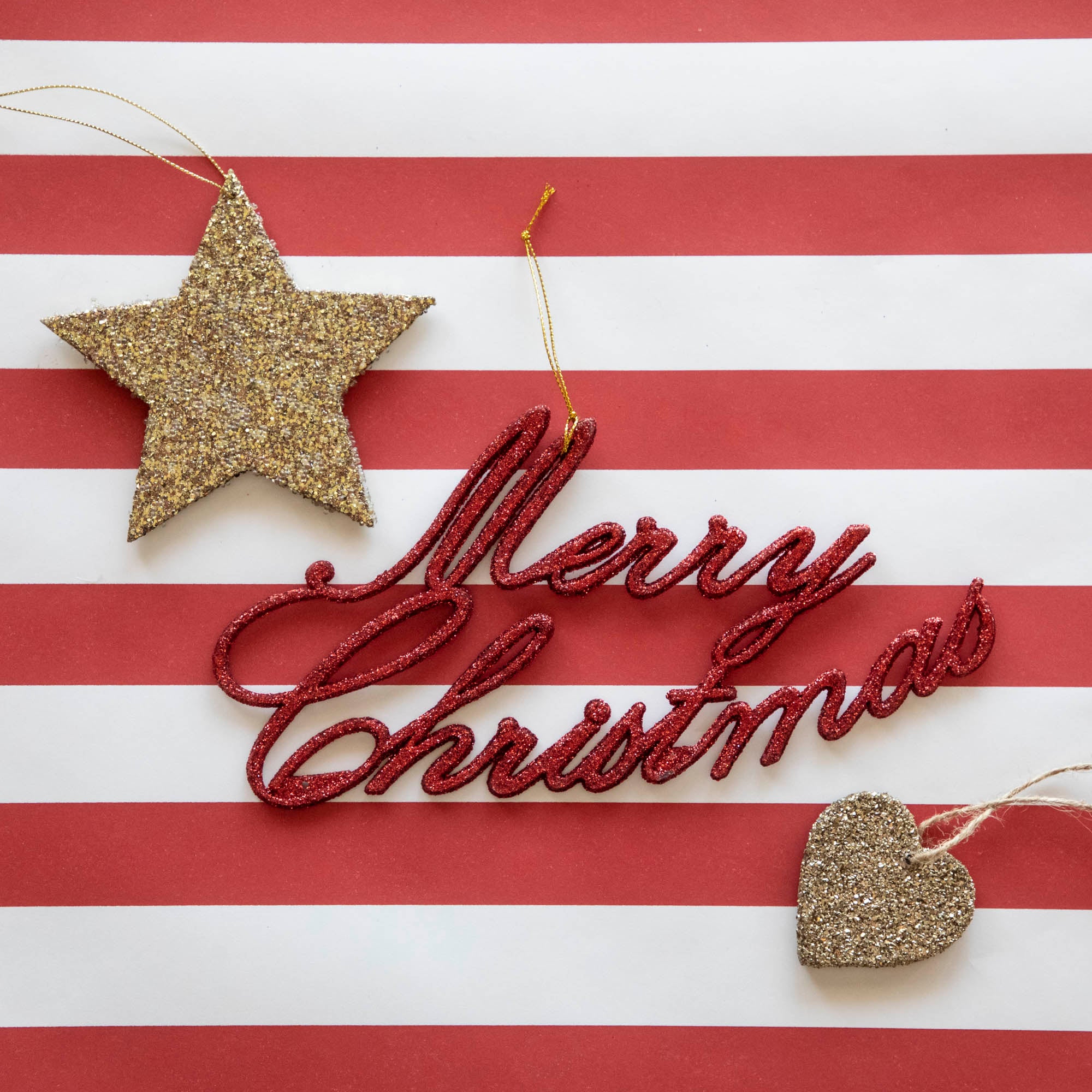 The Merry Christmas Ornament next to a glittery star and heart ornament, on the Red Classic Stripe Runner.