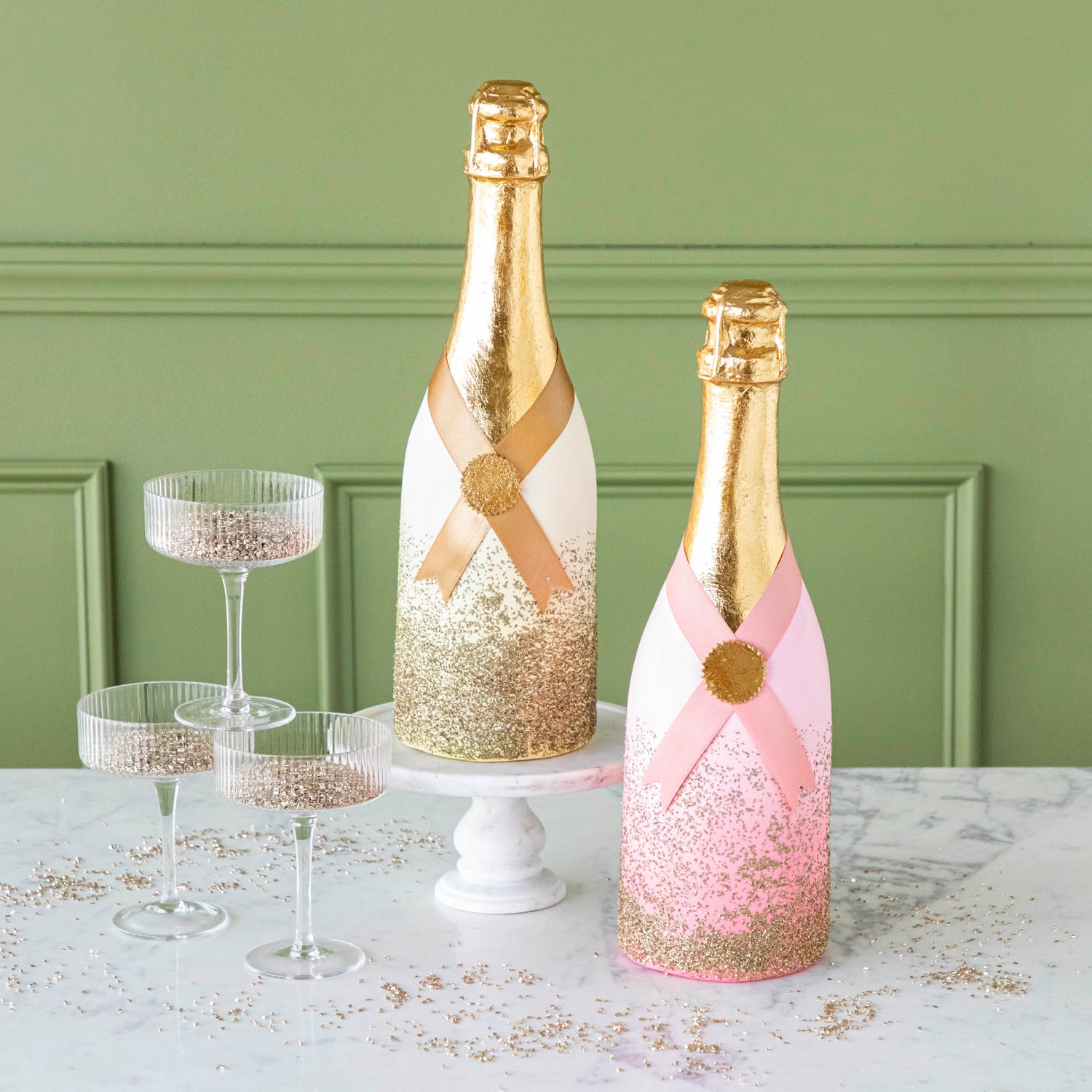 Pink and gold papermache Oversized Champagne Bottles, styled with coupe glasses filled with glitter.