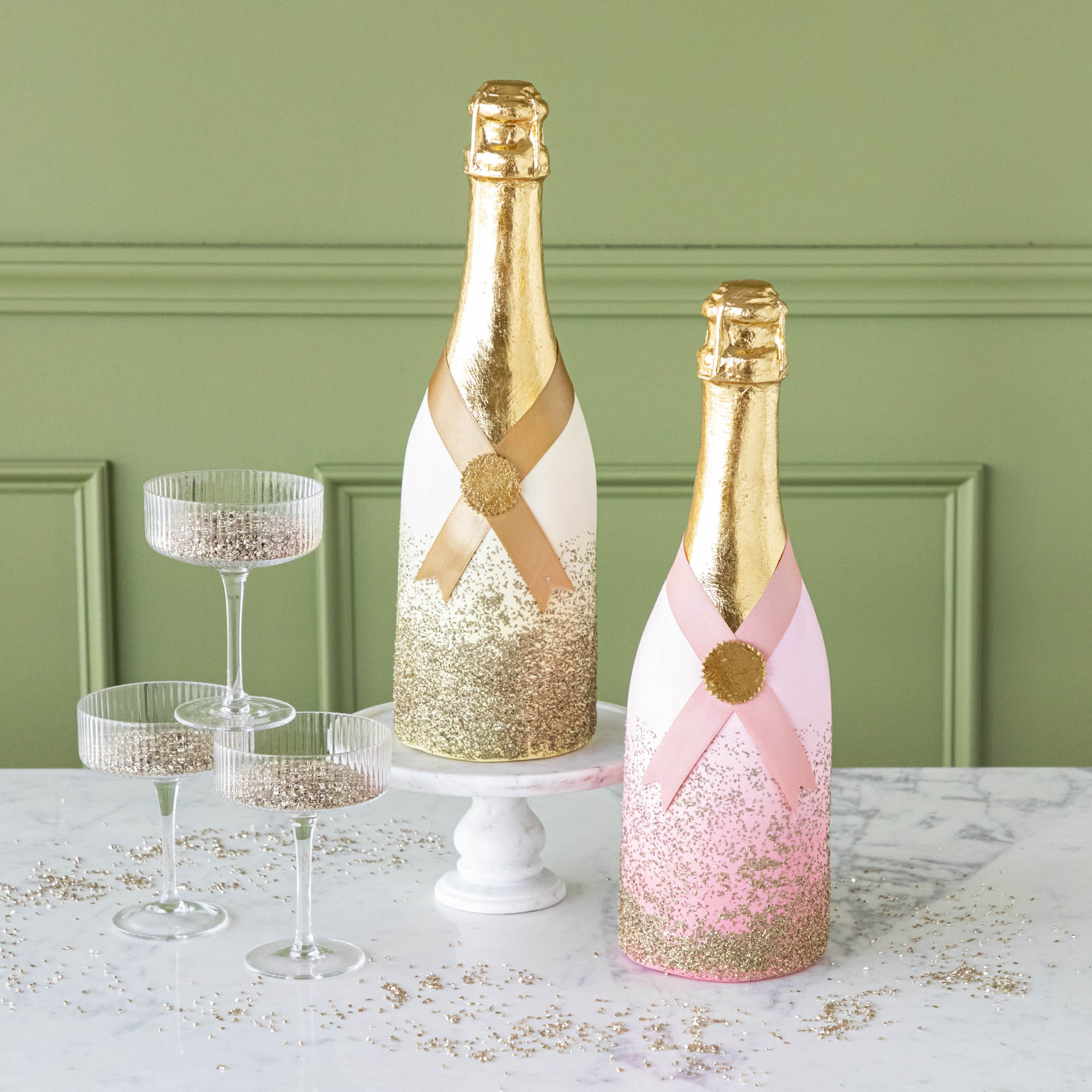 Pink and gold papermache Oversized Champagne Bottles, styled with coupe glasses filled with glitter.