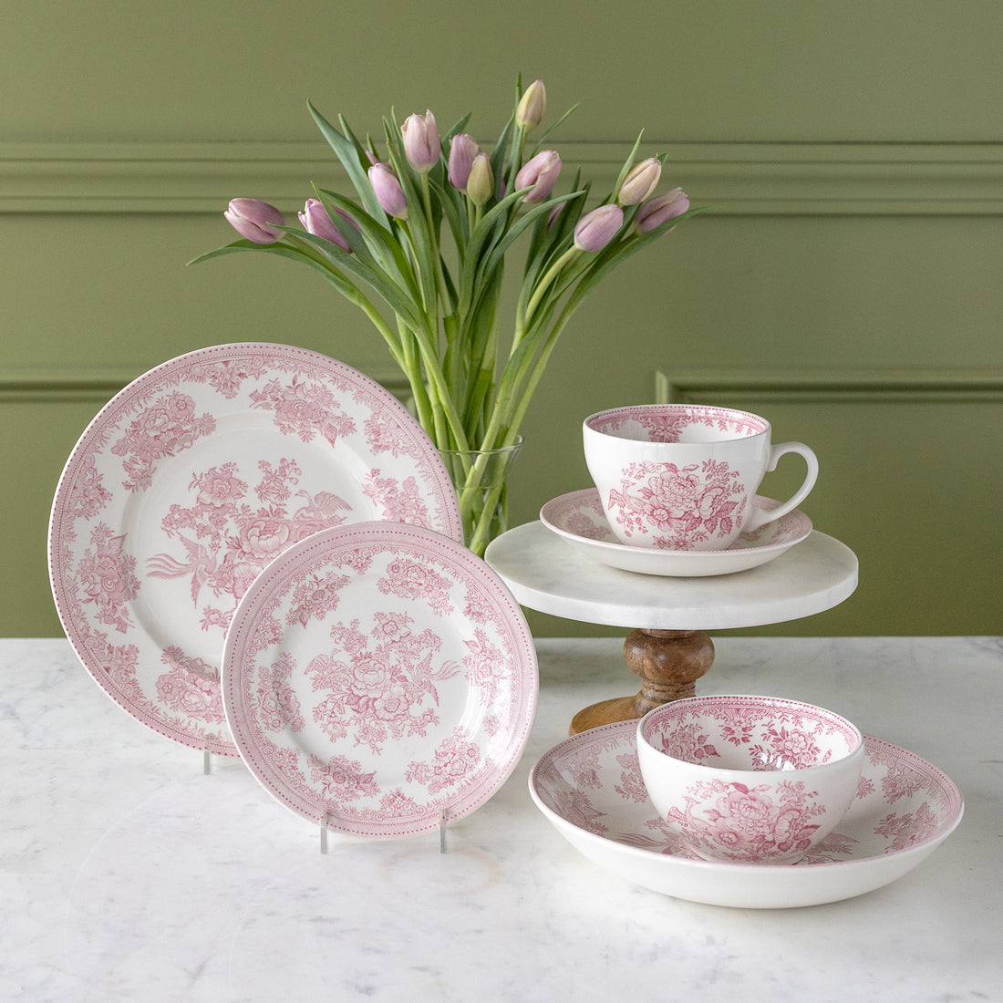 Burleigh Pink Asiatic Pheasants Dinnerware propped up with a vase of pink tulips behind them.