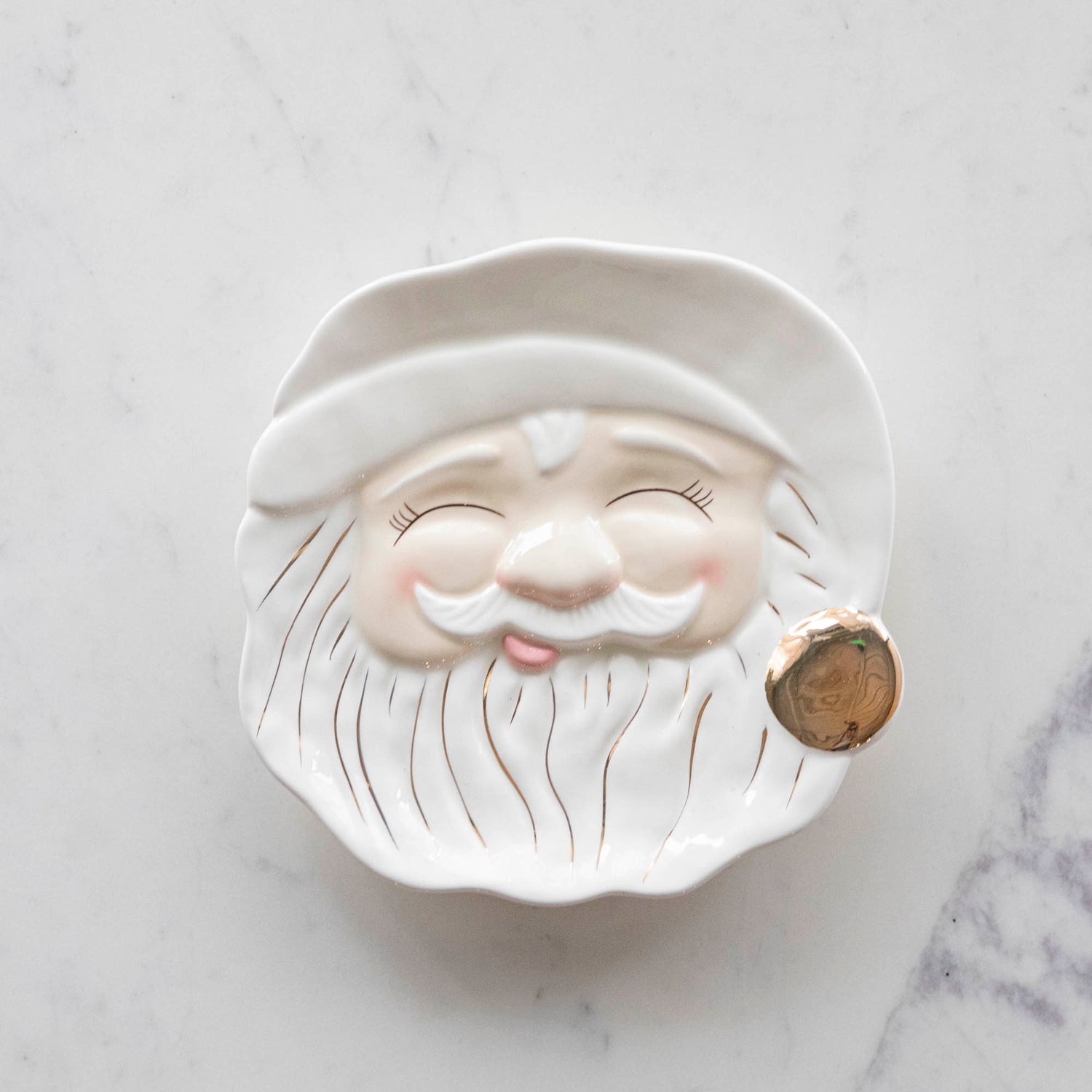 The Papa Noel Cream Cookie Plate with his eyes closed, a jolly face, rosy cheeks and hand-painted gold details.