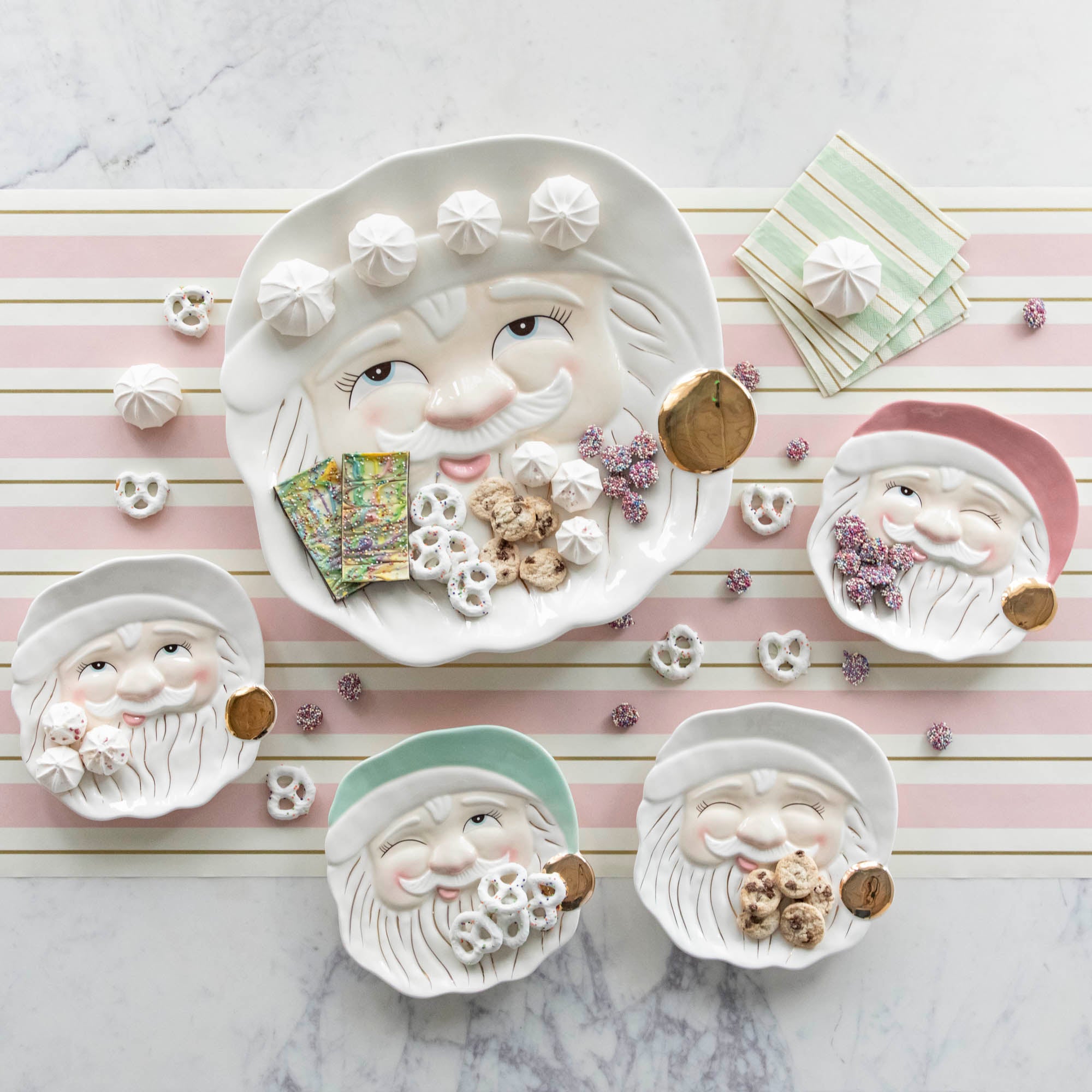 Papa Noel cream, mint and pink cookie plates with treats on them, next to the Papa Noel Cookie Platter, on the Pink &amp; Gold Awning Stripe Runner.