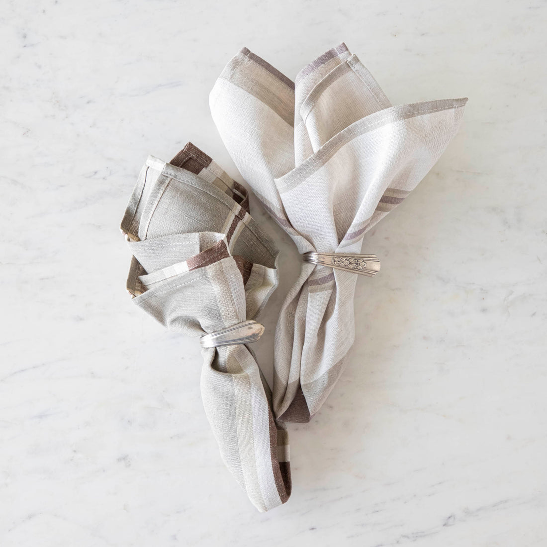 Oak Stone Cloth Napkin and Dusty Pastel Stripe Cloth Napkin in vintage silver napkin rings on a marble table.