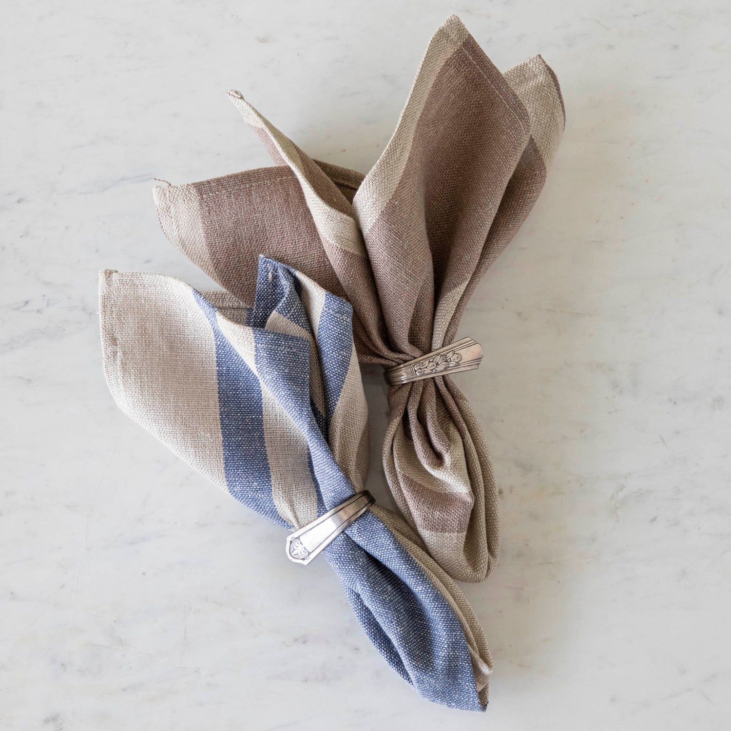 Dusty Rose Striped Woven Linen Napkin and Vintage Blue Striped Woven Linen napkin in vintage silver napkin rings on a marble table.