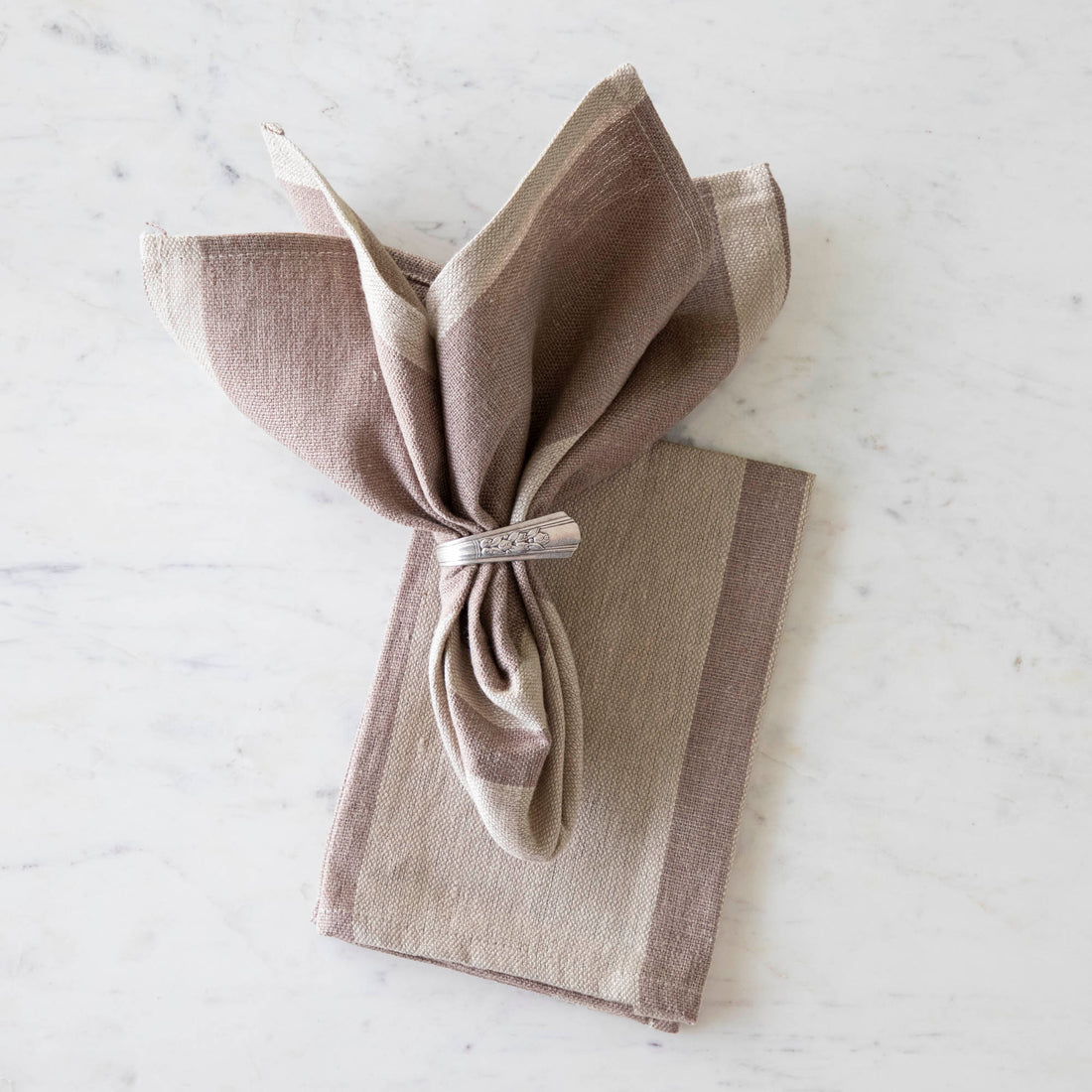 Dusty Rose Striped Woven Linen Napkin in a vintage silver napkin holder on top of the same napkin on a marble table.