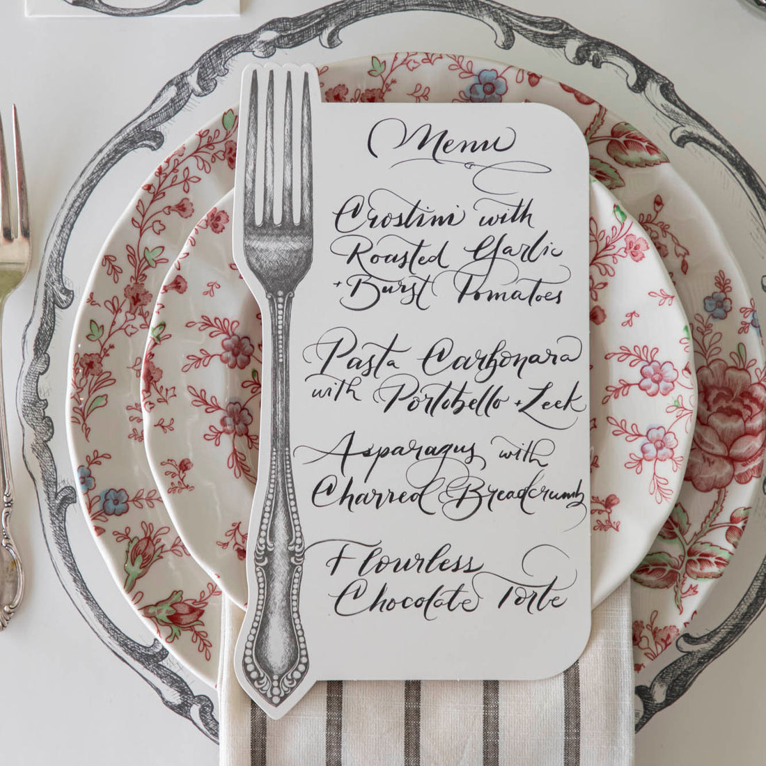 Vintage Fork Table Card with a menu written on it, resting on dinner plates on a table setting for one.