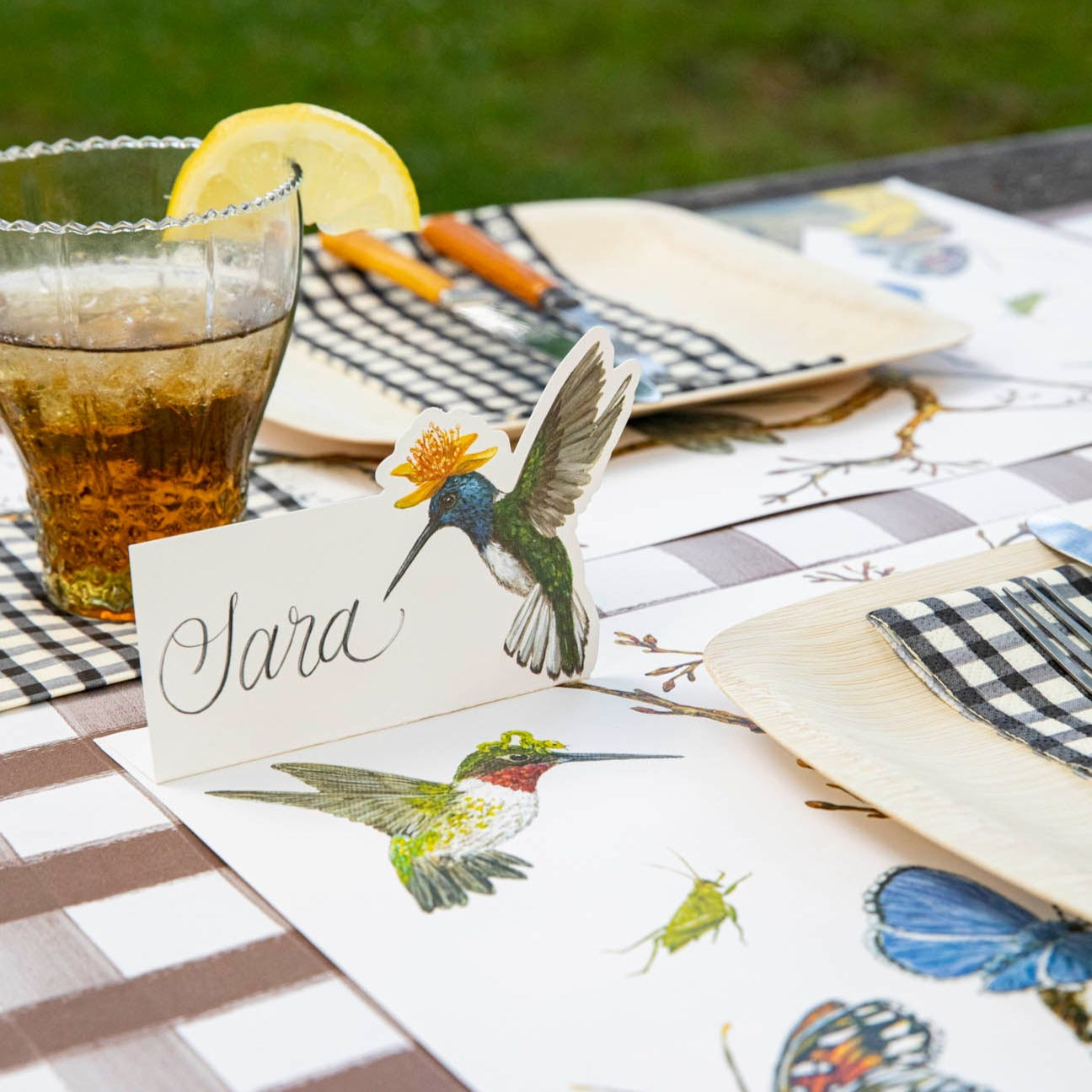 A Hummingbird Place Card labeled &quot;Sara&quot; standing on a picnic table setting.