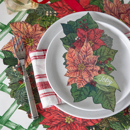 The Die-cut Poinsettia Placemat on the Green Lattice Runner,  featuring the Poinsettia Table Accent with &quot;Toby&quot; written on it, resting on a plate.