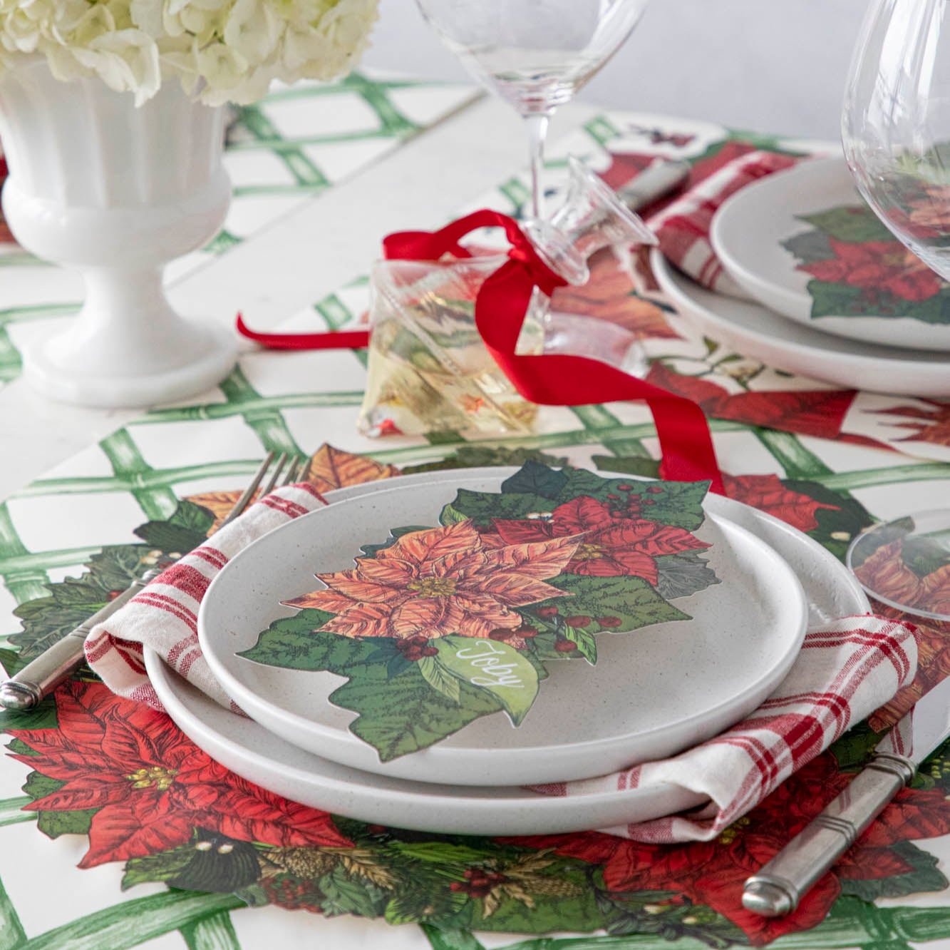 An elegant table setting with flowers, featuring the Die-cut Poinsettia Placemat on the Green Lattice Runner, with the Poinsettia Table Accent resting on a plate.