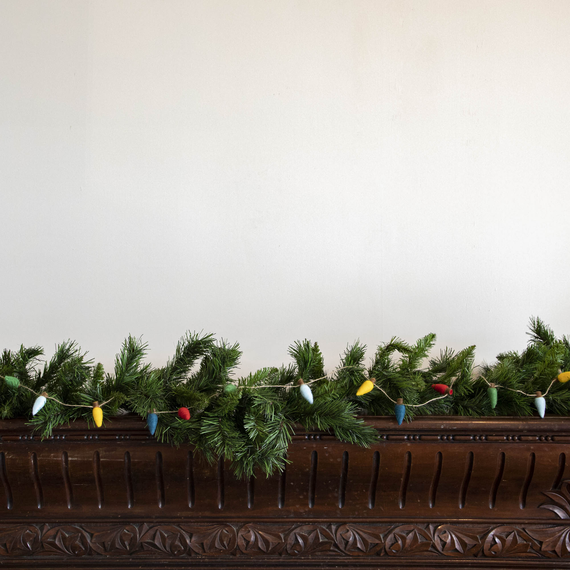 Felt String of Lights hanging on garland, propped on a mantle.