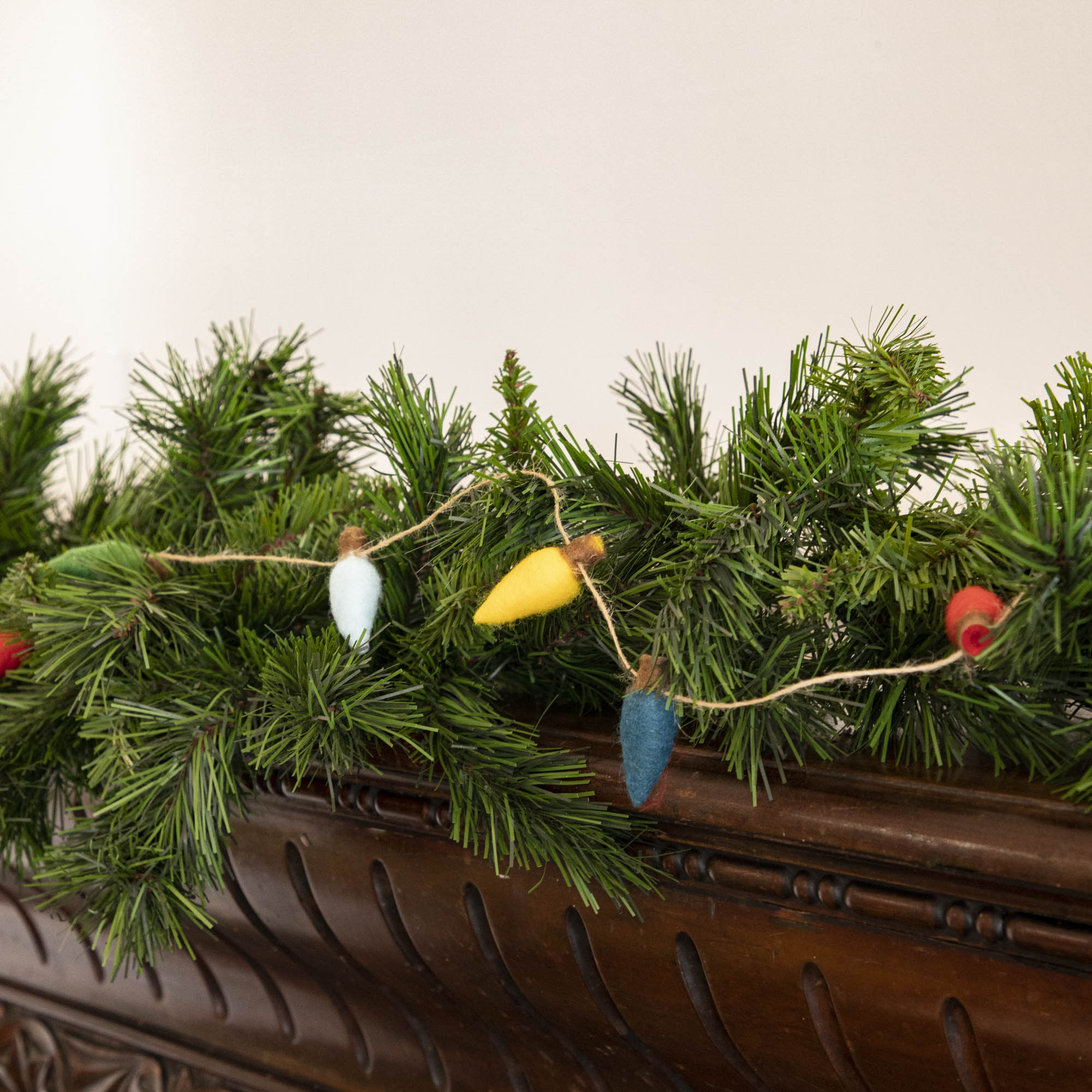 Felt String of Lights hanging on garland, propped on a mantle.