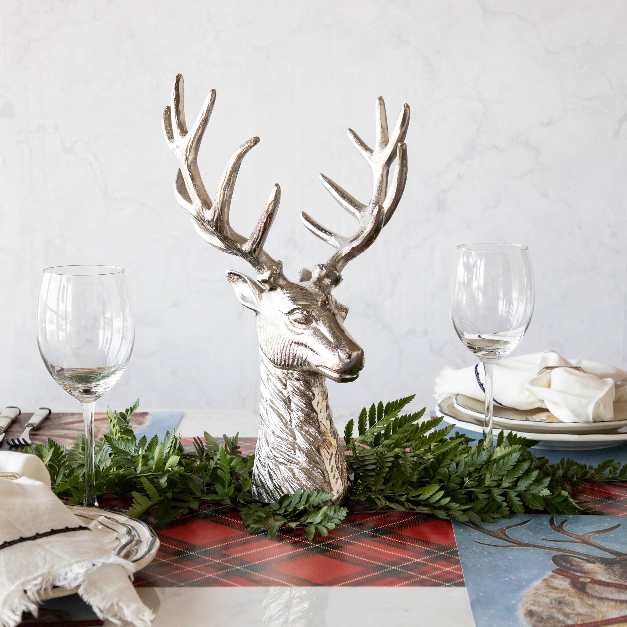 An aluminum Reindeer Bust, in the center of a woodland themed table setting, surrounded by a leaf garland.