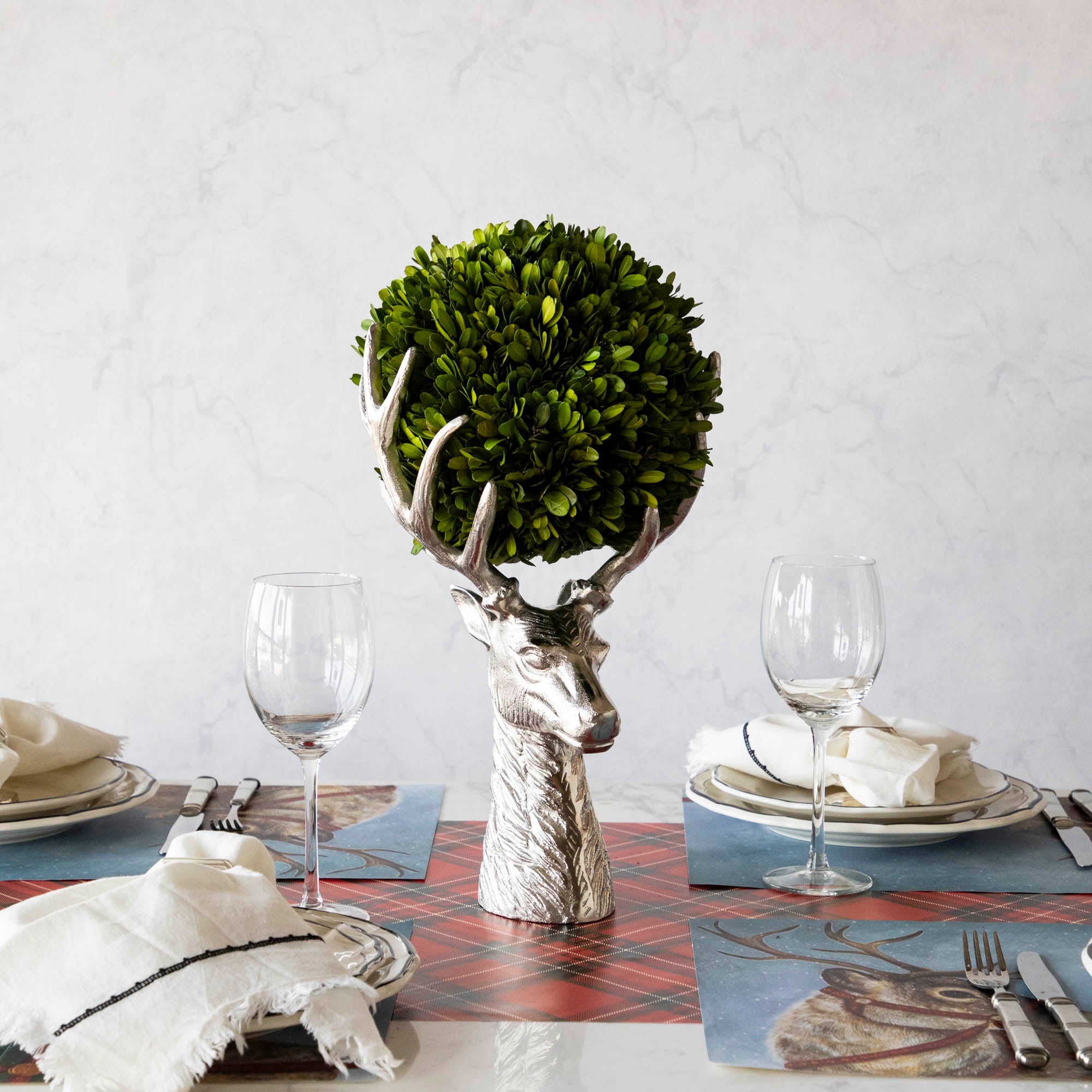 An aluminum Reindeer Bust, in the center of a woodland themed table, holding a boxwood ball between its antlers.