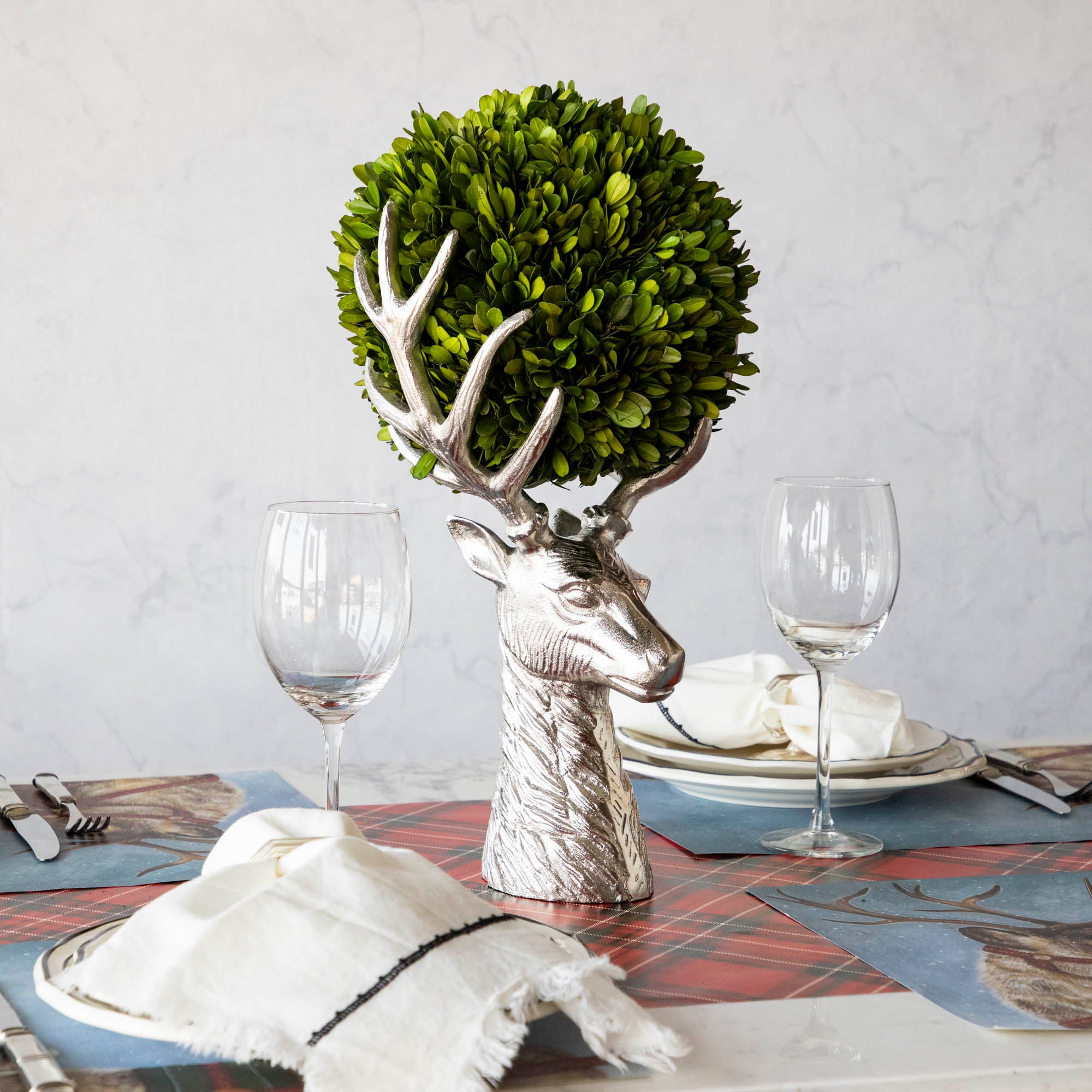 An aluminum Reindeer Bust, in the center of a woodland themed table, holding a boxwood ball between its antlers.