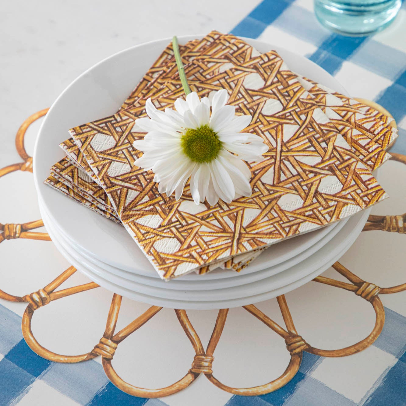 Rattan Weave Serving Paper under a stack of small plates with Rattan Weave Napkins and a flower on top.