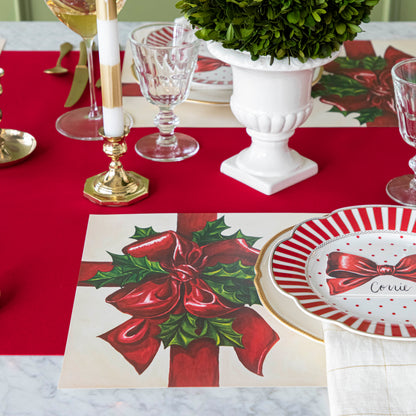 An elegant Christmas themed table setting with the Red Flocked Runner underneath the Christmas Present Placemat, glassware, candles and an urn with a boxwood ball inside.