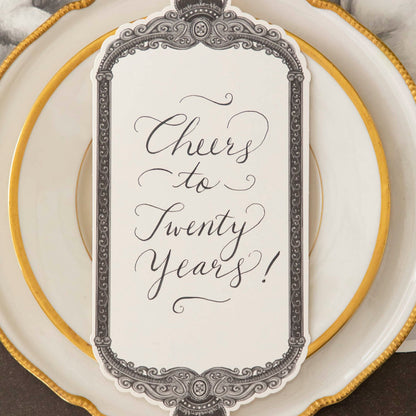 Regal Frame Table Card with &quot;Cheers to Twenty Years!&quot; written on it, resting on dinner plates.