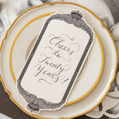 Regal Frame Table Card with &quot;Cheers to Twenty Years!&quot; written on it, resting on dinner plates.