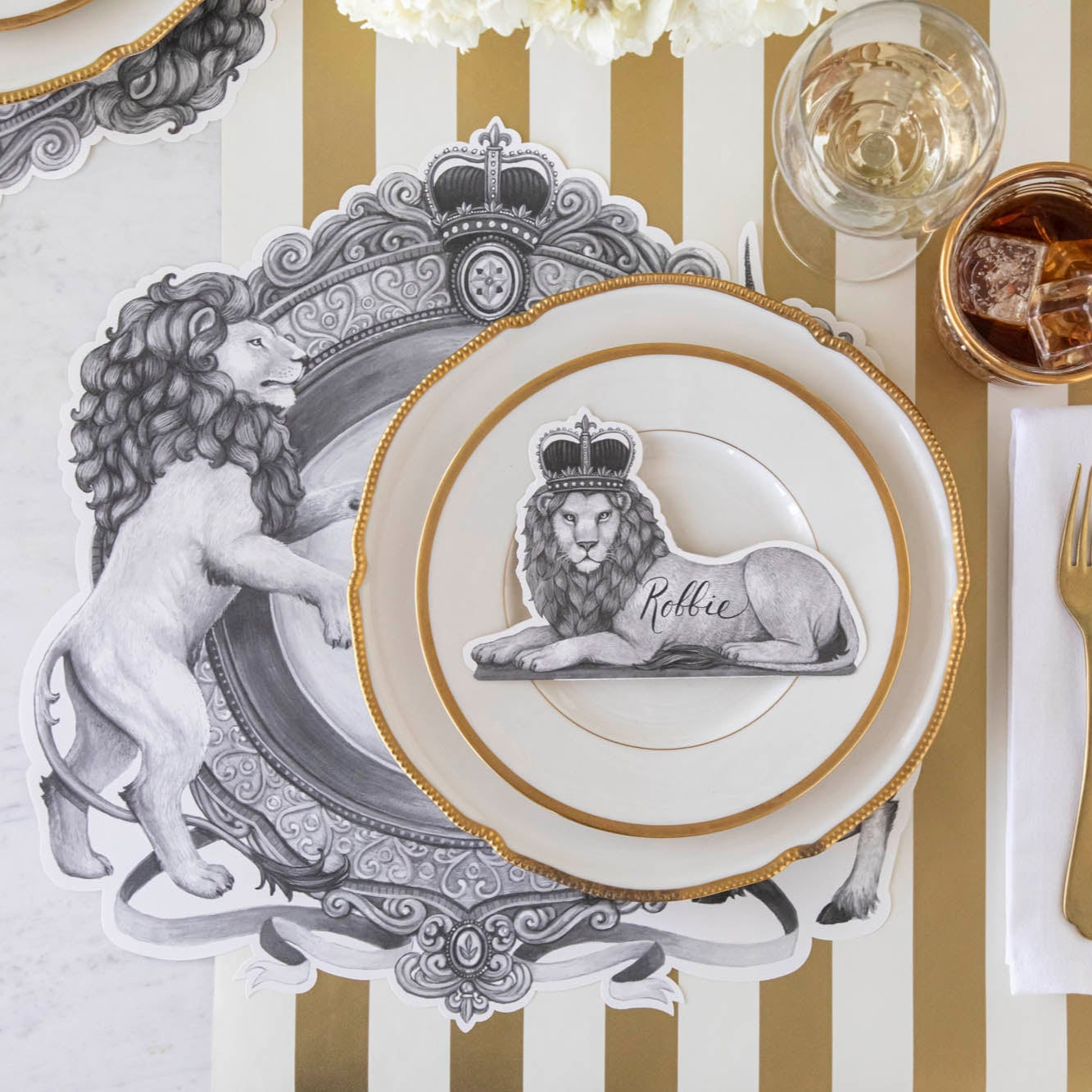 Regal Lion Place Card with &quot;Robbie&quot; written on it, resting on dinner plates on top of the H&amp;C Regal Crest Placemat.