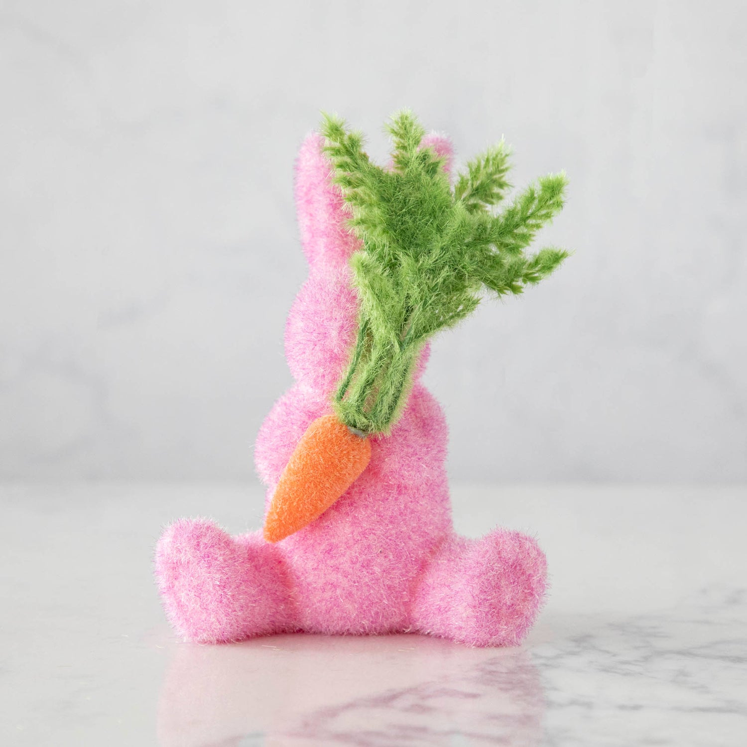 A Glitterville Flocked Bunny holding a bunch of carrots, perfect for Easter.