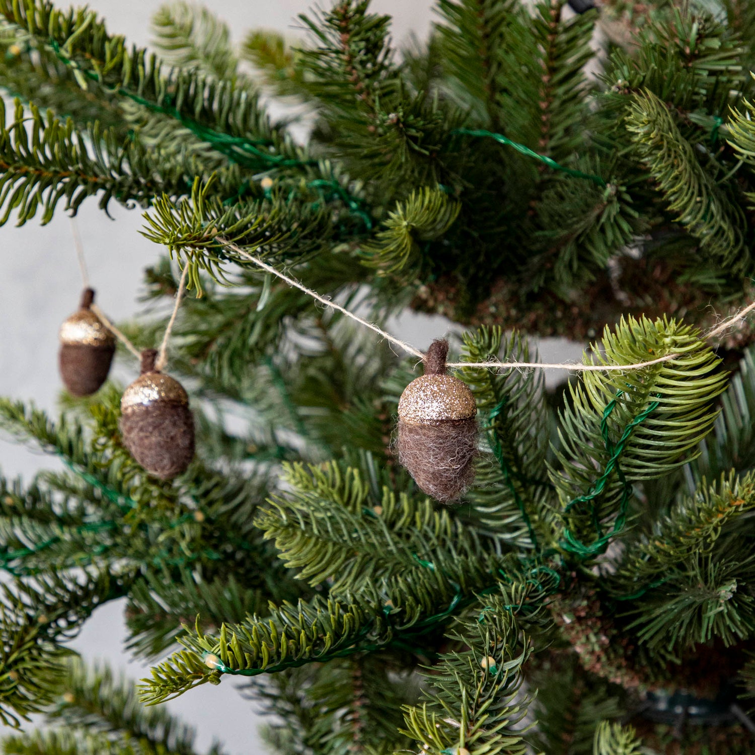 Close up of woolen acorn garland in a tree showing its glittered top 