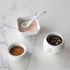 Three White Porcelain Mini Bowls with assorted spices and a spoon on a marble surface by BIA.