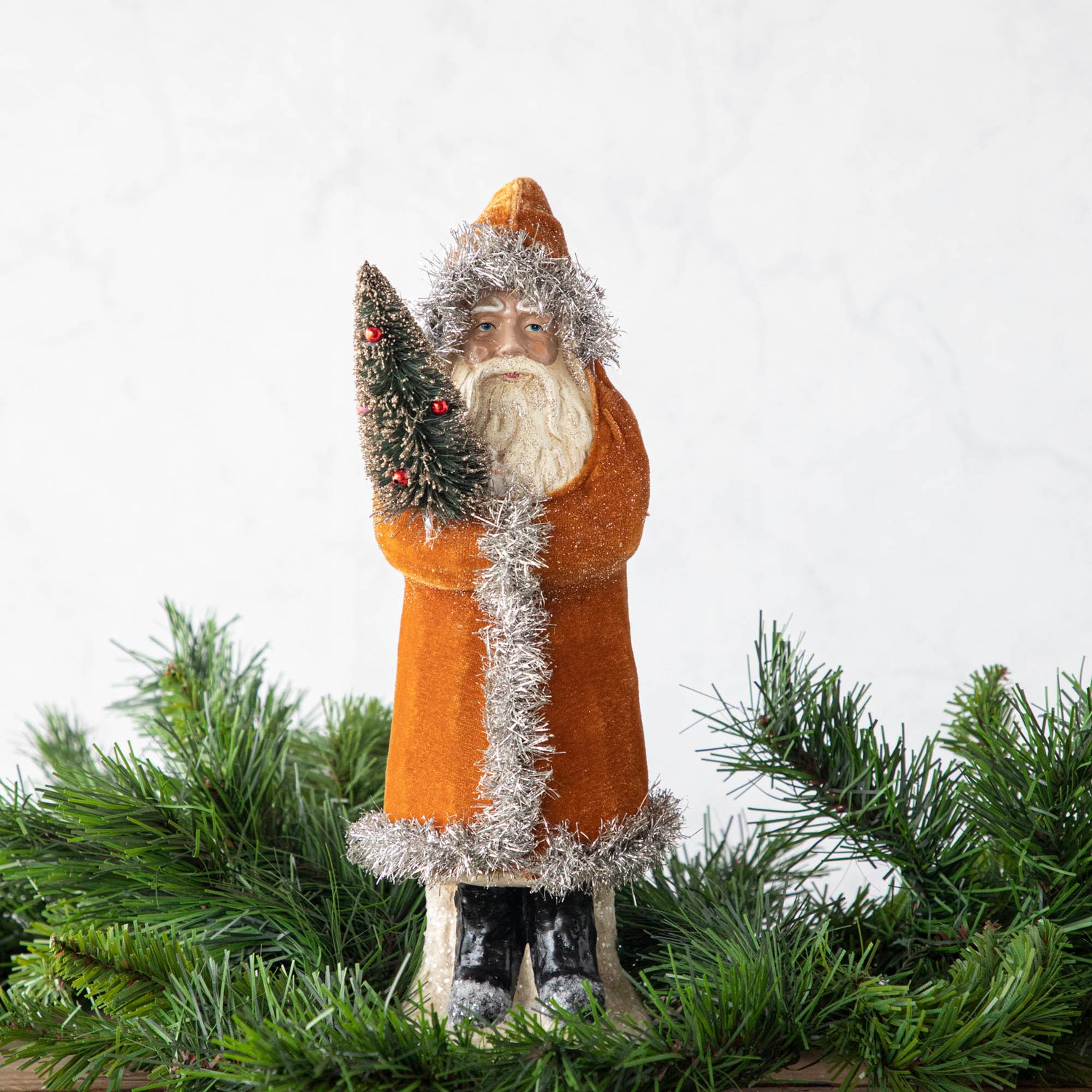 A 12&quot; Velvet Belsnickle figurine with a gold velvet robe adorned with tinsel trimming and glitter, holding a tree.