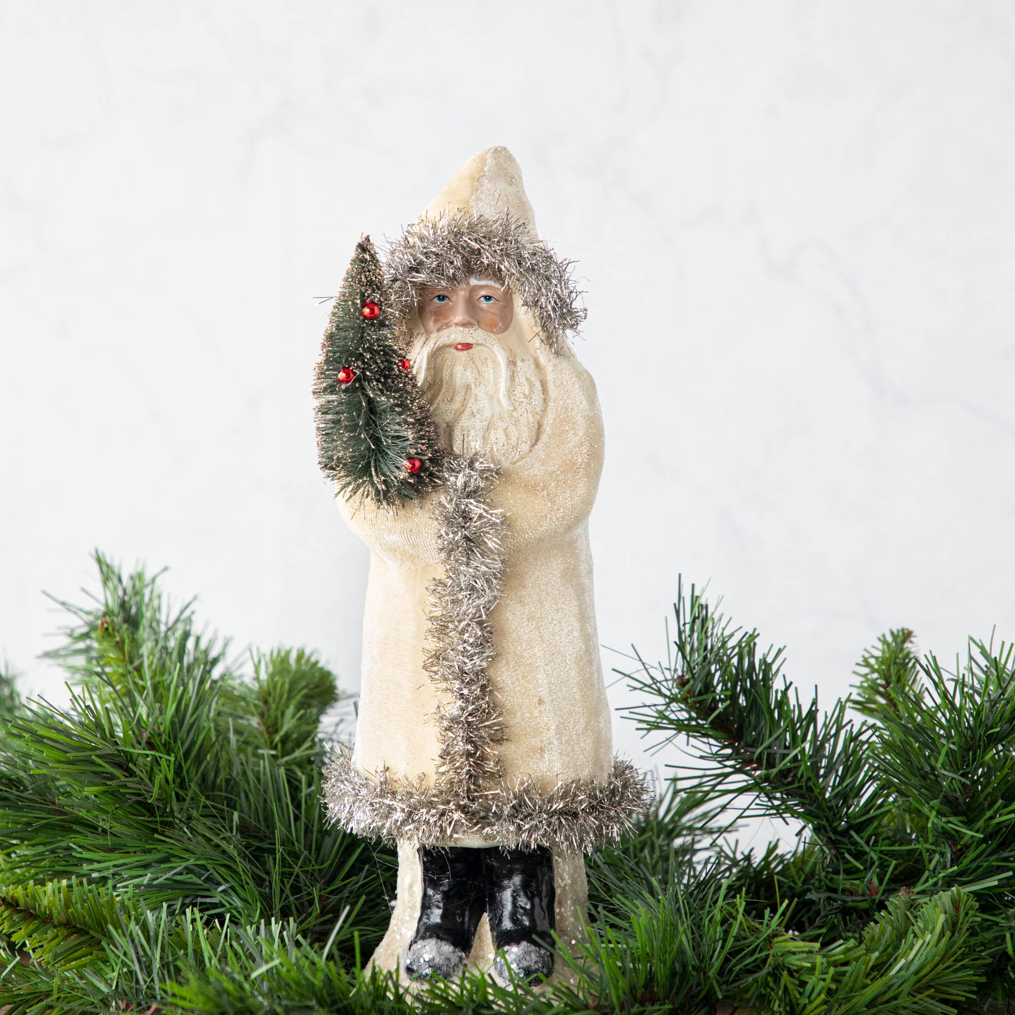 A 12&quot; Velvet Belsnickle figurine with a white velvet robe adorned with tinsel trimming and glitter, holding a tree.