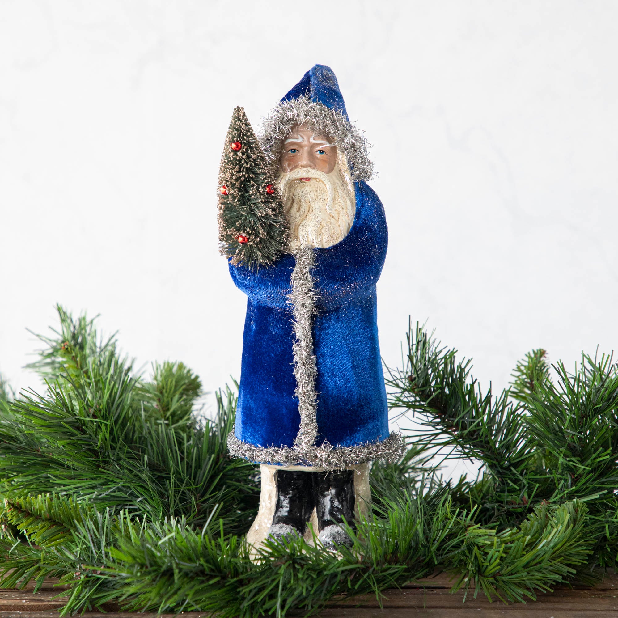 A 12&quot; Velvet Belsnickle figurine with a navy velvet robe adorned with tinsel trimming and glitter, holding a tree.