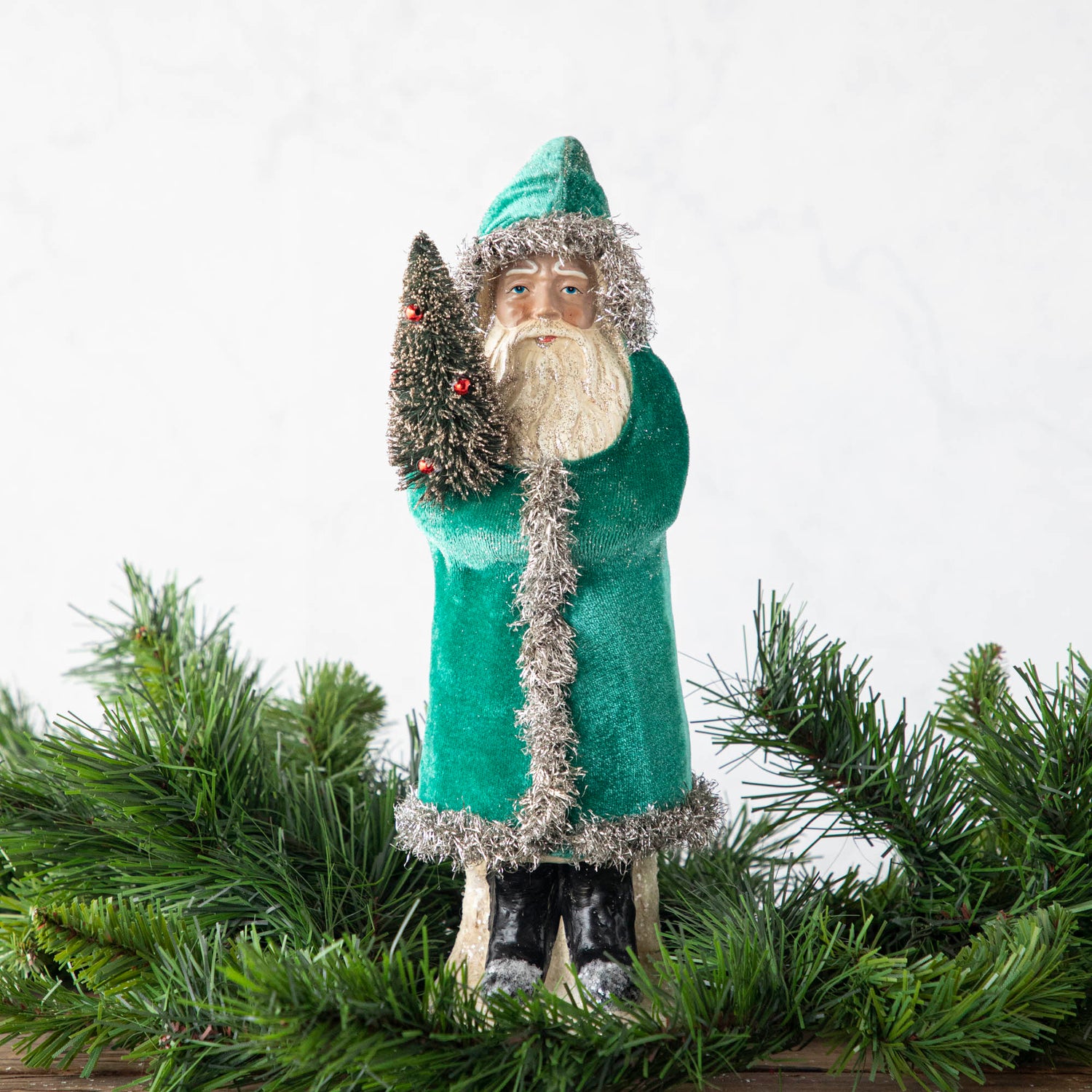 A 12&quot; Velvet Belsnickle figurine with a teal velvet robe adorned with tinsel trimming and glitter, holding a tree.