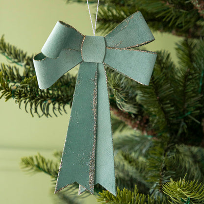 close up of green bow ornament hanging in a tree