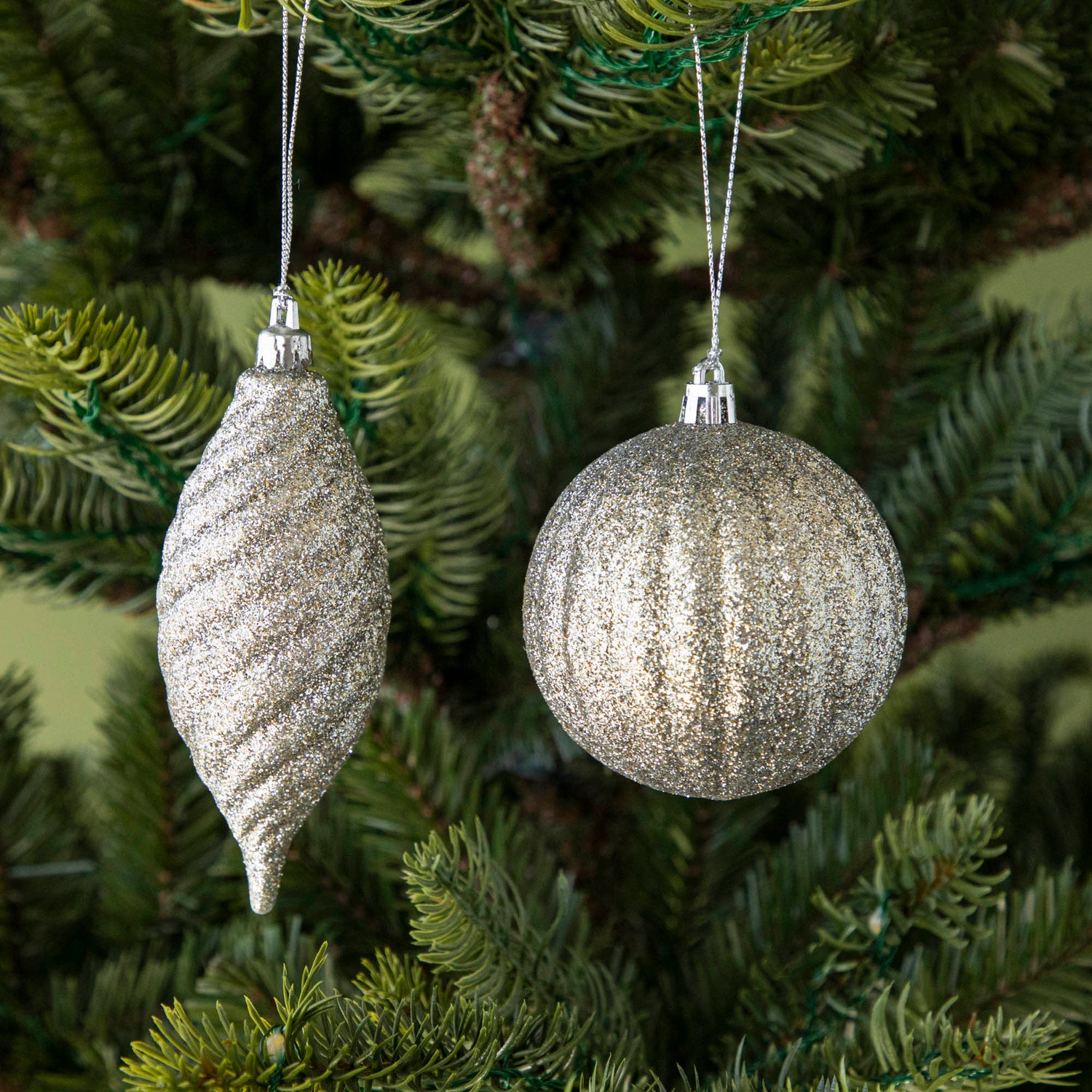 Round and drop shape silver glittered ornaments hanging on a tree.