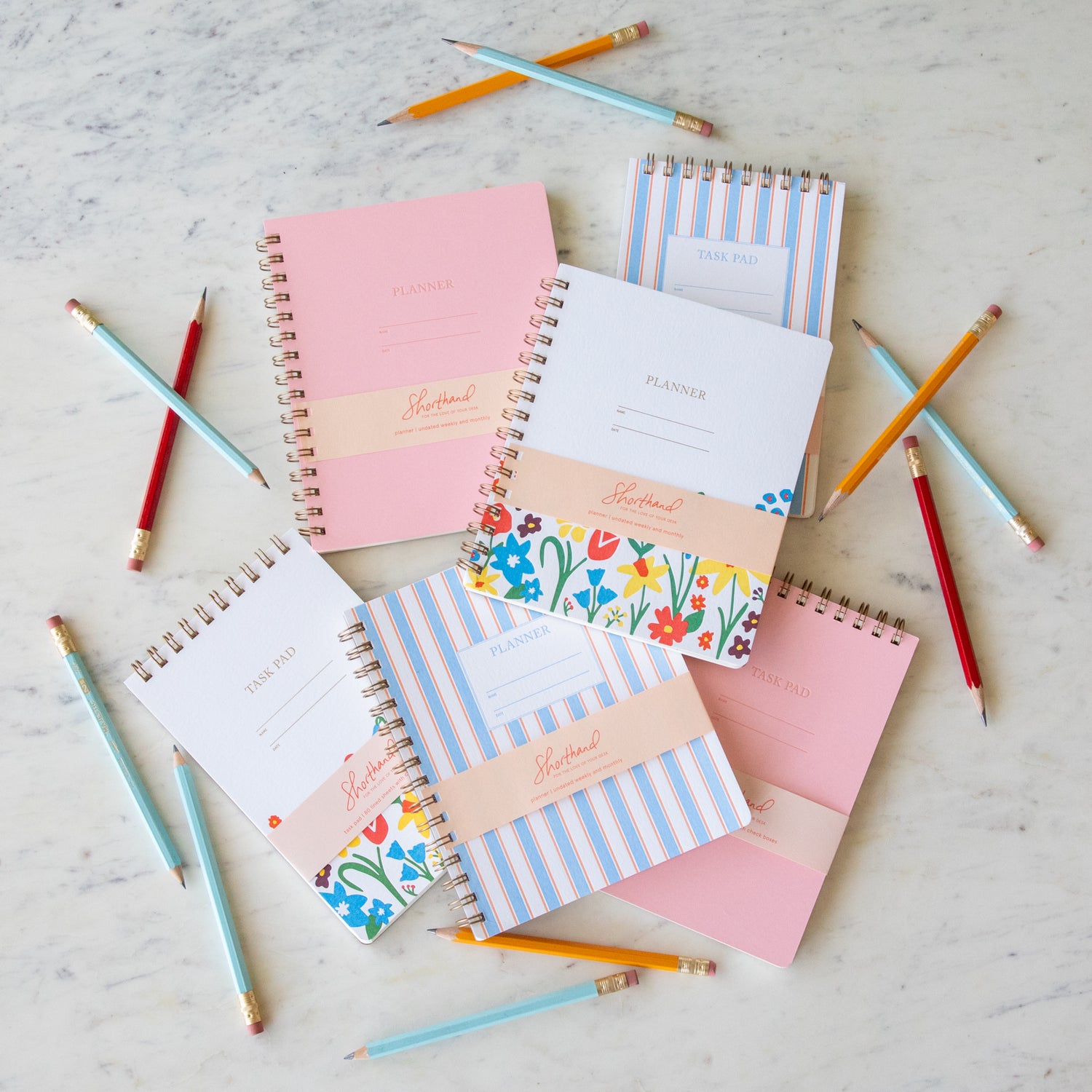 A flat lay of Undated Letterpress Planners and Task Pads by Shorthand Press overlapping each other on a table surrounded by pencils.