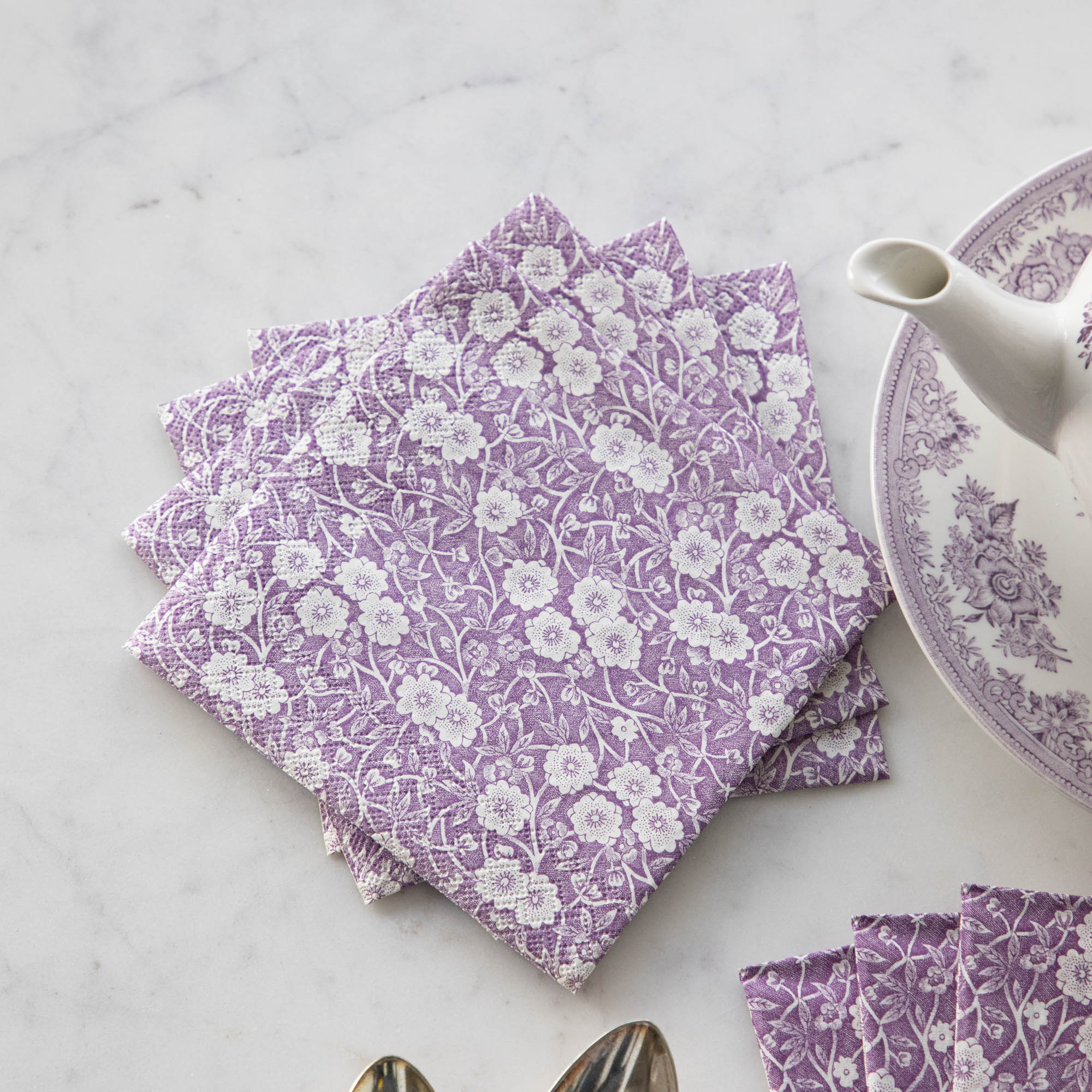 A set of beautiful Lilac Calico Napkins by Hester &amp; Cook exquisitely decorated on a table next to a teapot.