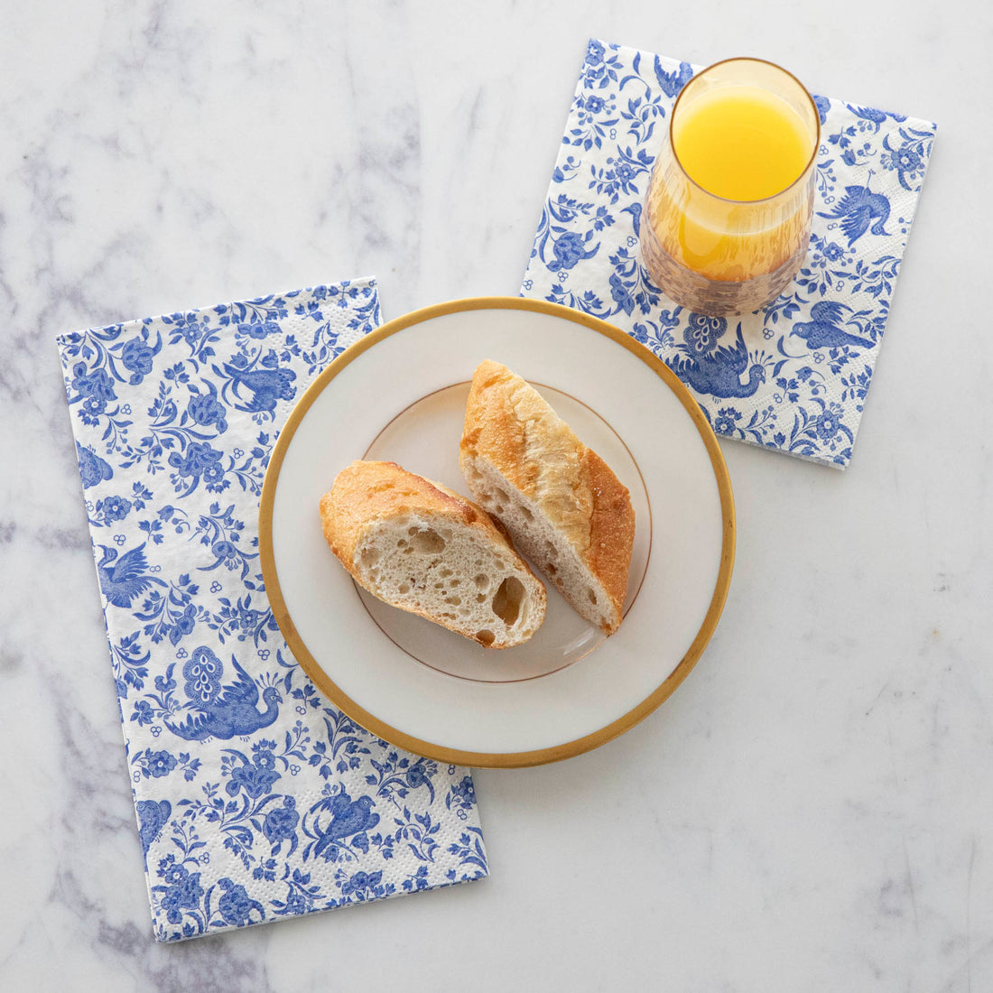 A plate of bread and a glass of juice on top of Blue Regal Peacock Guest and Cocktail Napkins by Hester &amp; Cook.