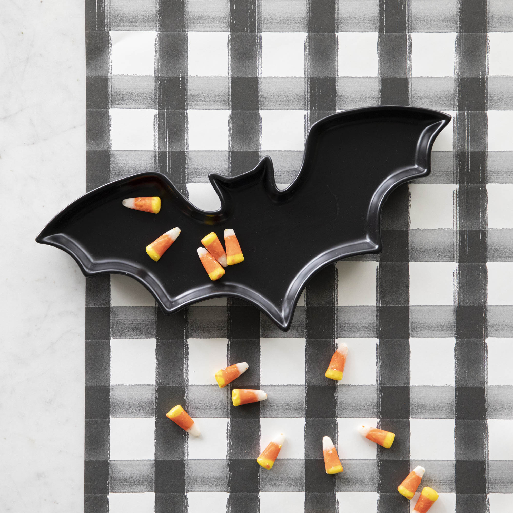 Black Stoneware Bat Shaped Plate with candy corn pieces sprinkled across, and the Black Painted Check Runner underneath.